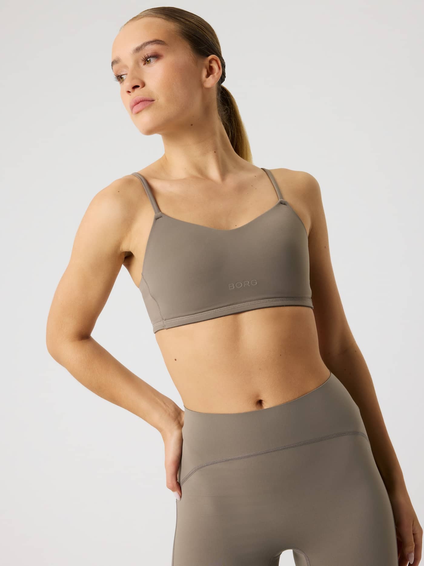 Front view of a woman wearing the brown Studio Soft Padded Bra with a brown logo, featuring a comfortable fit for training. - Image 6