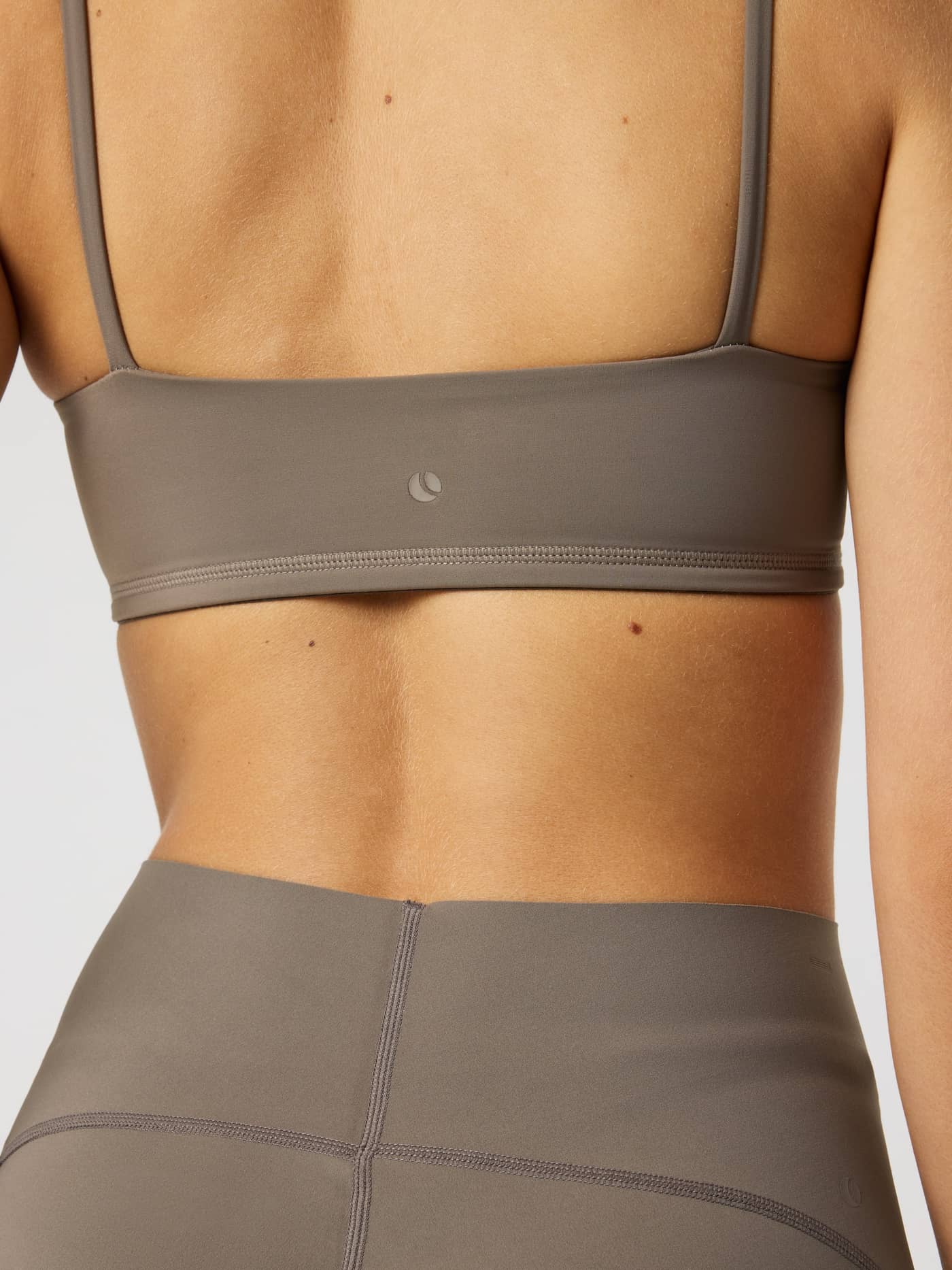 Back view of a model wearing the Studio Soft Padded Bra in Falcon (Brown), showing style and fit for training. - Image 4