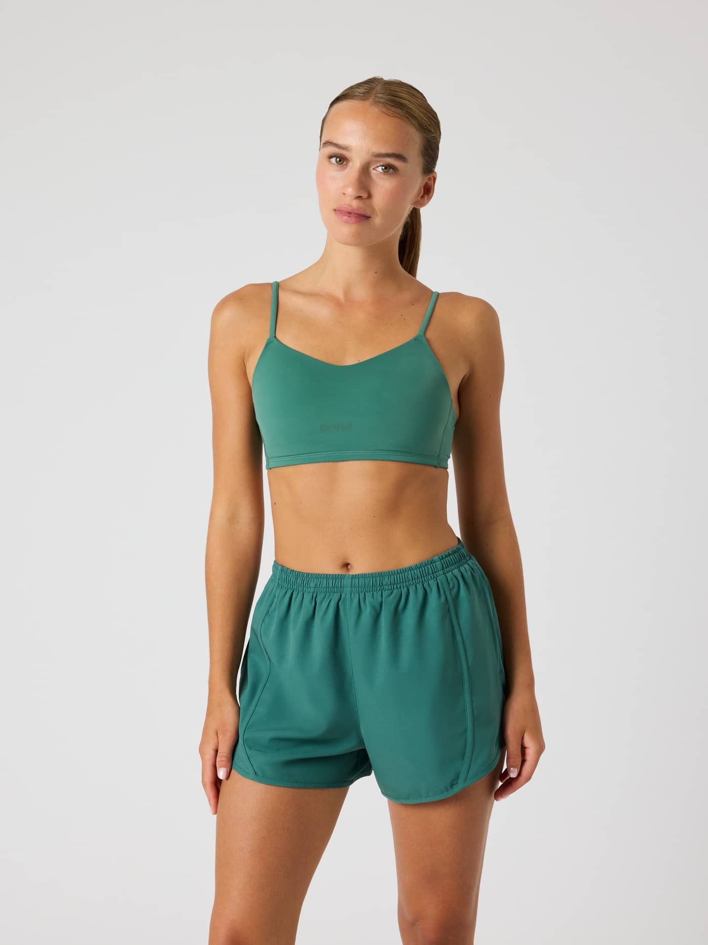 Front view of a model in the Mallard Green (Green) Studio Soft Padded Bra with a tonal logo, for training style and fit. - Image 1