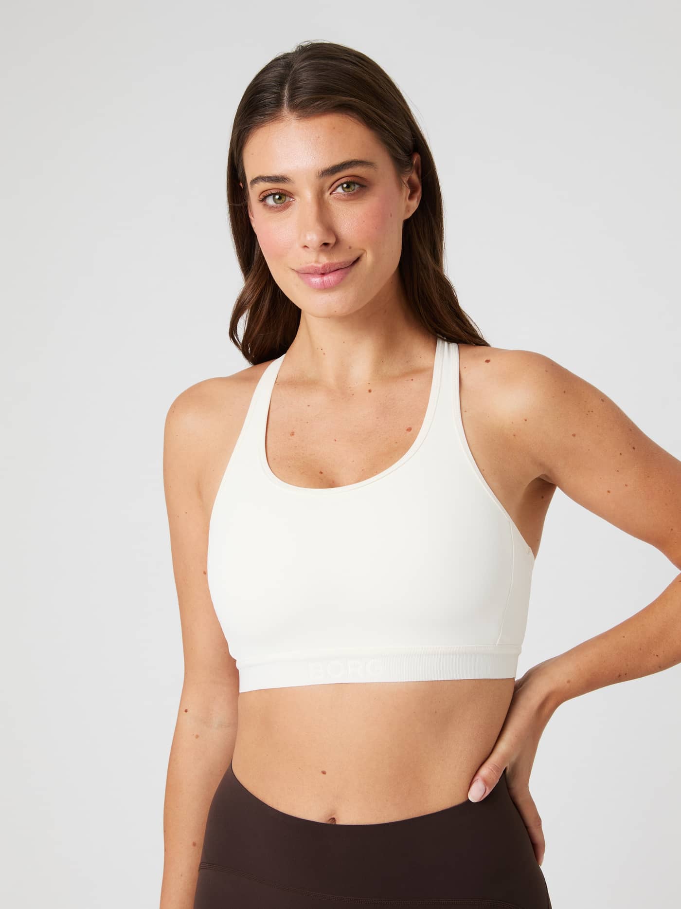 Front view of a woman wearing the white Borg Low Support Sports Bra with a white logo, designed for a stylish training fit. - Image 3
