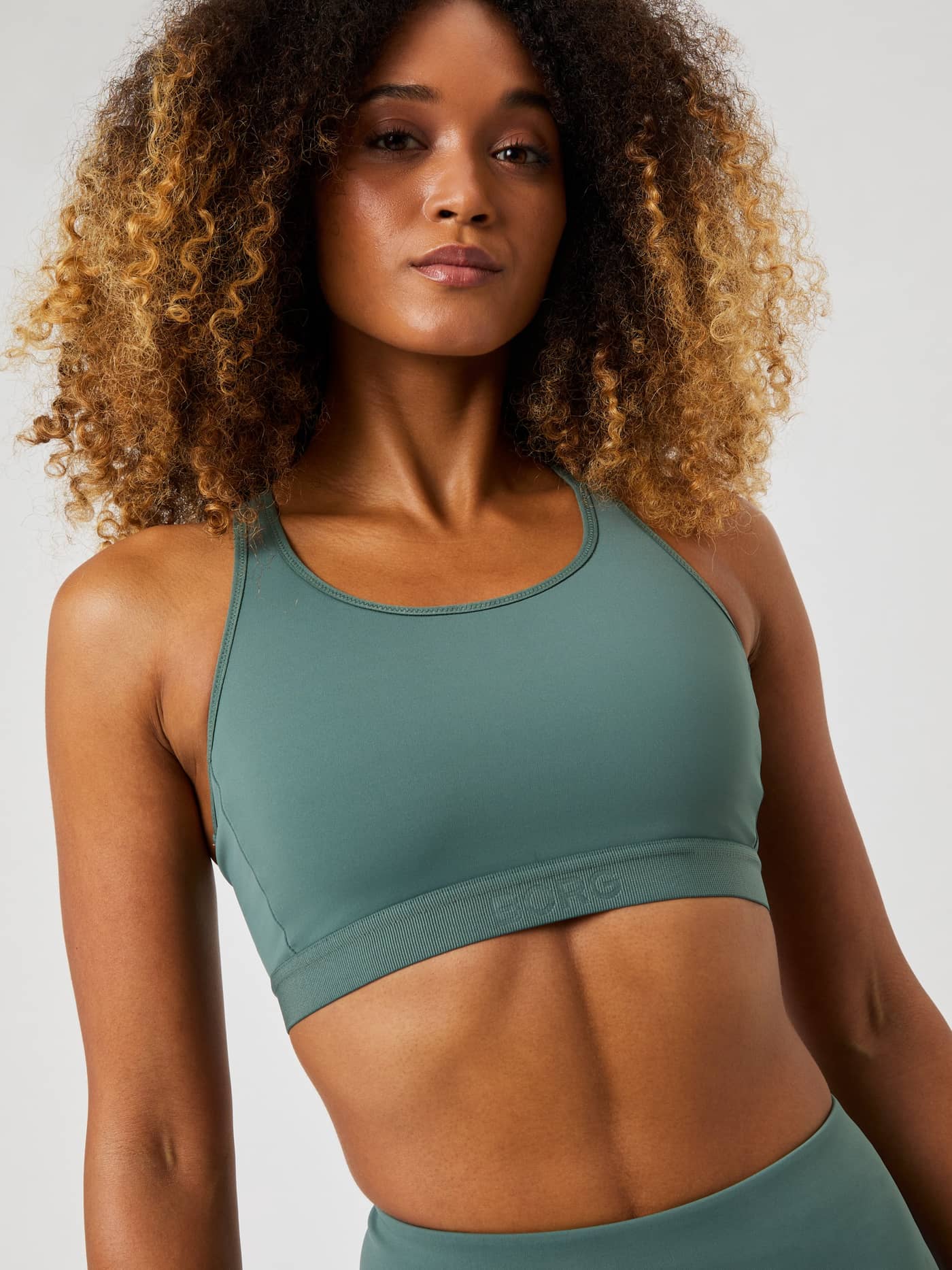 Front view of a model in the training-ready Borg Low Support Sports Bra in Balsam Green (Green) with a green embossed logo. - Image 3