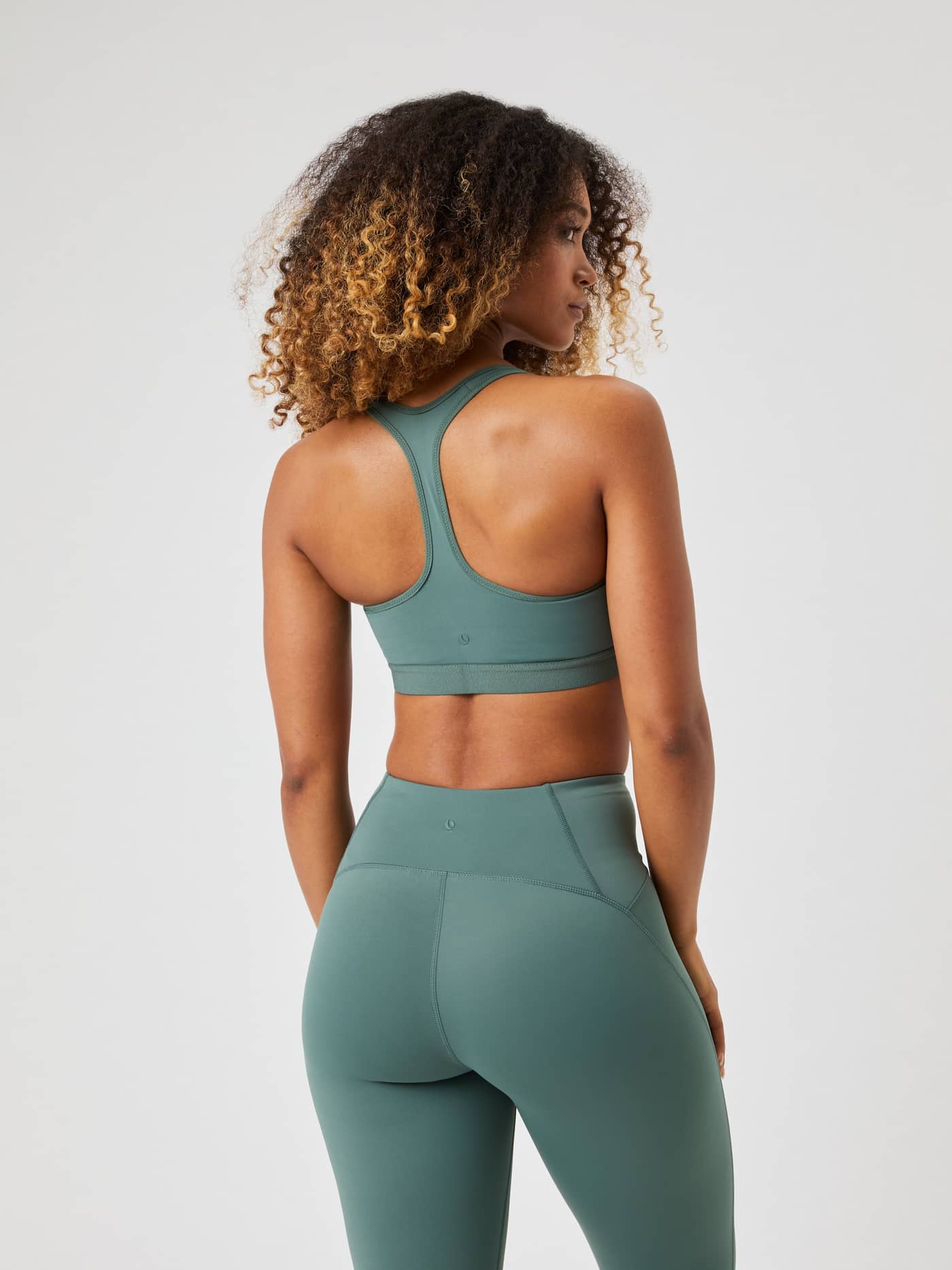 Back view of a woman in the Borg Low Support Sports Bra in Balsam Green (Green) and leggings for a stylish training fit. - Image 2