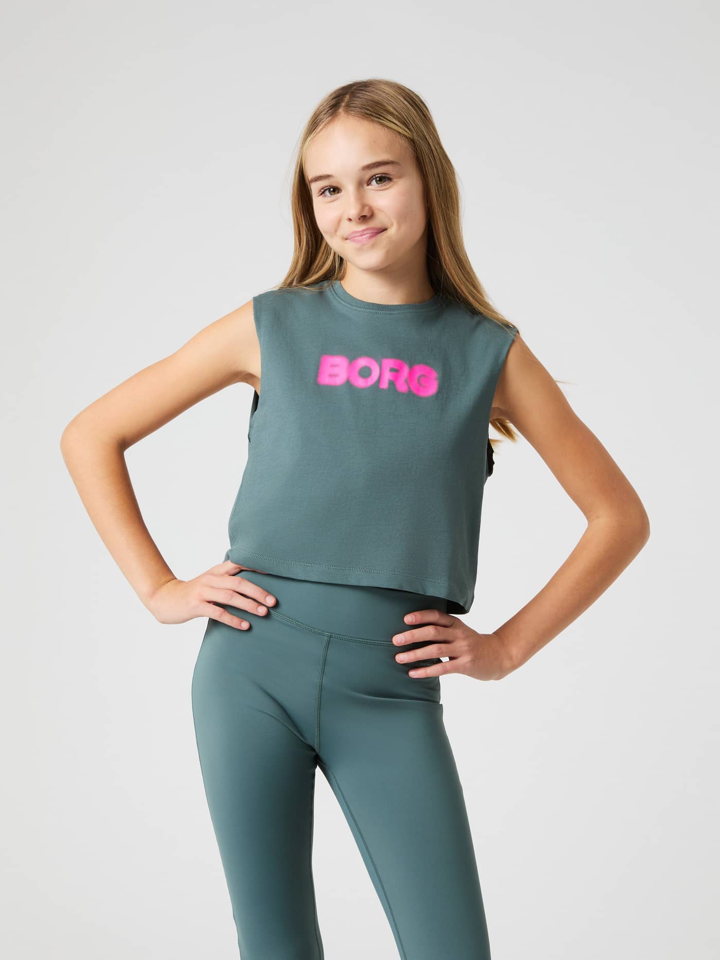 Front view of a kid in the Balsam Green (Green) Borg Cropped Tank Top with a pink logo for kids' cotton blend training. - Image 1