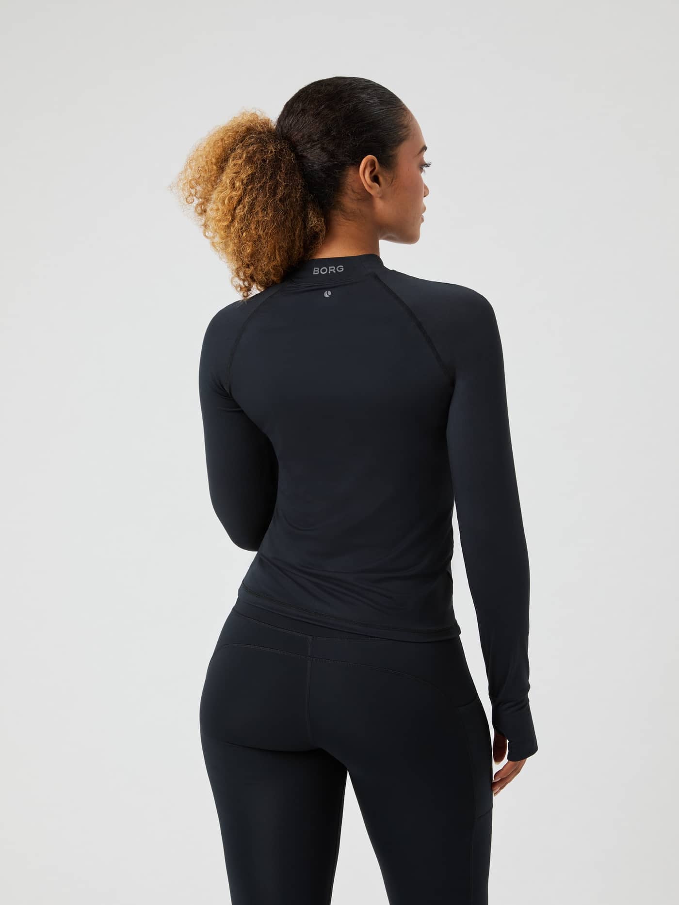 Back view of a woman in the Borg Performance Brushed Mockneck in Black Beauty (Black) with a grey logo for a running fit. - Image 2