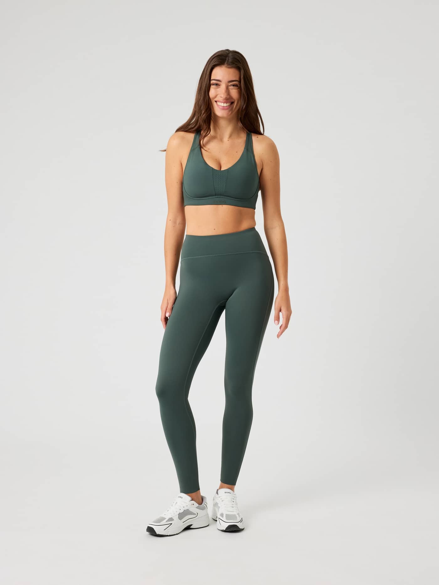 Full-body front view of a woman wearing the Urban Chic (Green) Borg Reform Tights and a matching sports bra for training. - Image 3