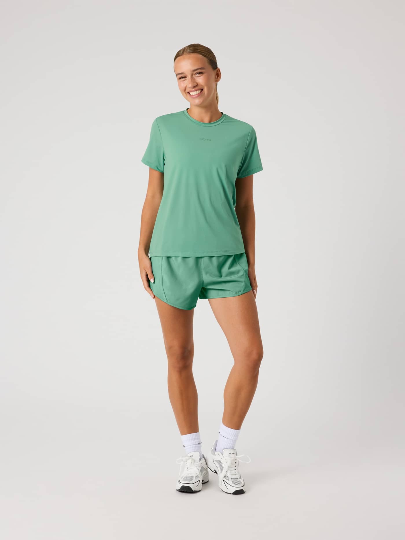 Full-body front view of a woman wearing the Malachite Green (Green) Borg Sports T-Shirt for performance training or tennis. - Image 3