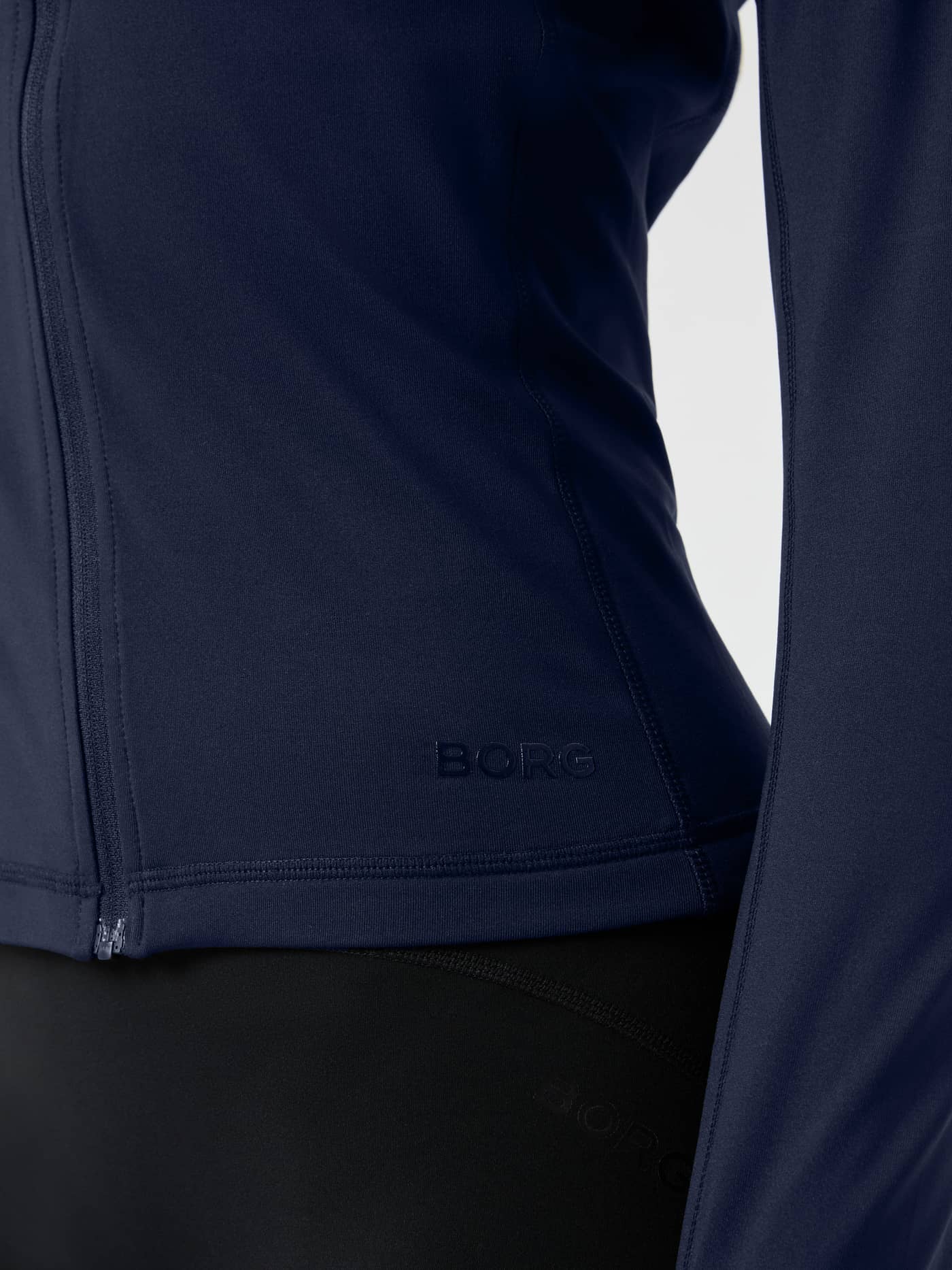 Close-up of a woman wearing the Björn Borg Full Zip Midlayer in Night sky (Navy) for training, showing the tonal navy logo. - Image 5
