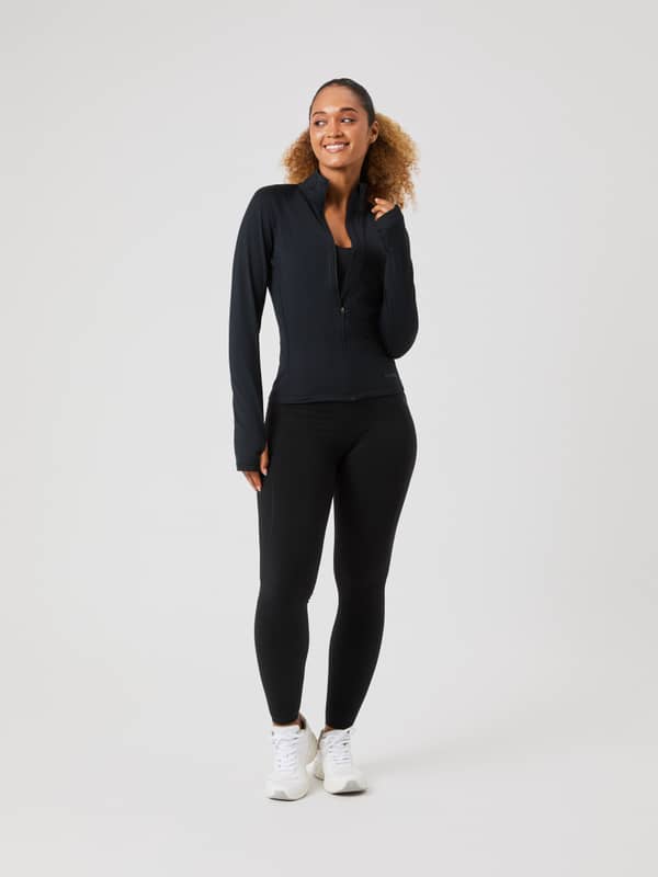 Ganzkörperansicht einer Frau im Borg Full Zip Midlayer in Black Beauty (Schwarz) und passenden Leggings für das Training.