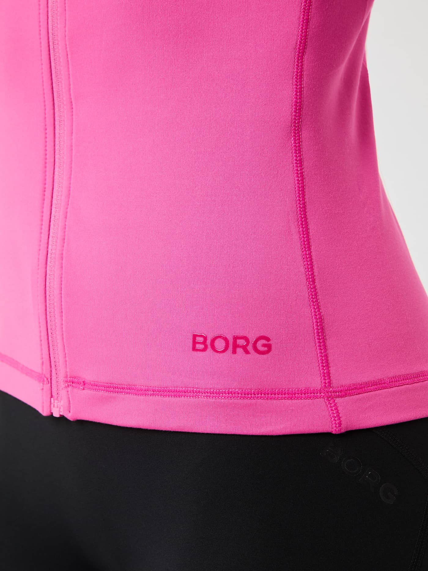 Borg Full Zip Midlayer i Ibis Rose (Lyserød) set i nærbillede med fokus på logoet ved sømmen til træning. - Image 5
