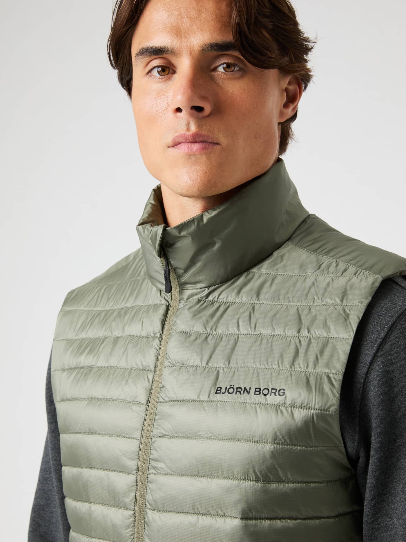 Närbild framifrån på en man i funktionella Borg Light Padded Vest i Dusty Olive (Grön) med svart logotyp. - Image 1