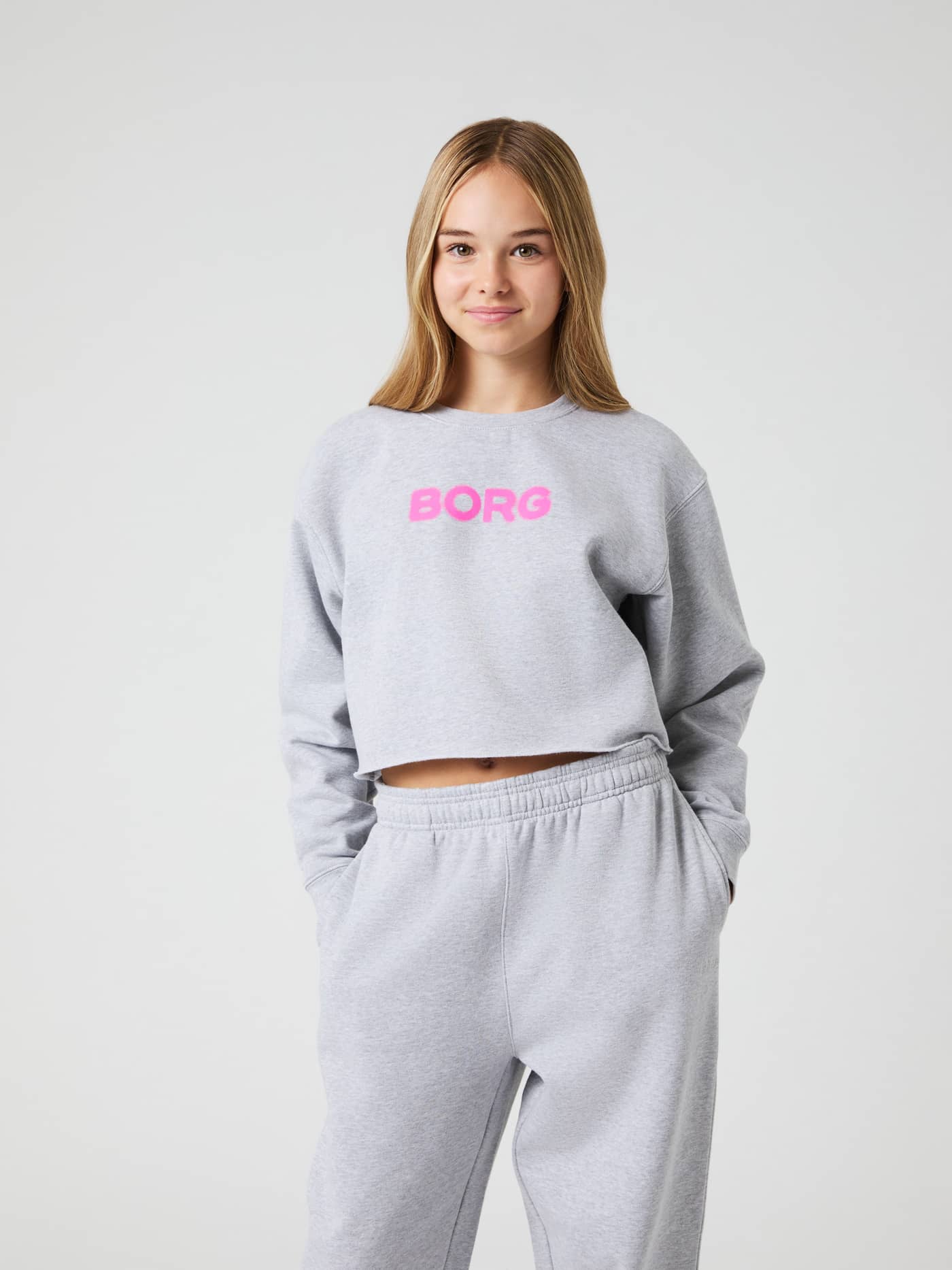Front view of kids wearing the Light Grey Melange (Grey) Borg Oversized Cropped Sweatshirt with a pink logo and raw hem. - Image 1