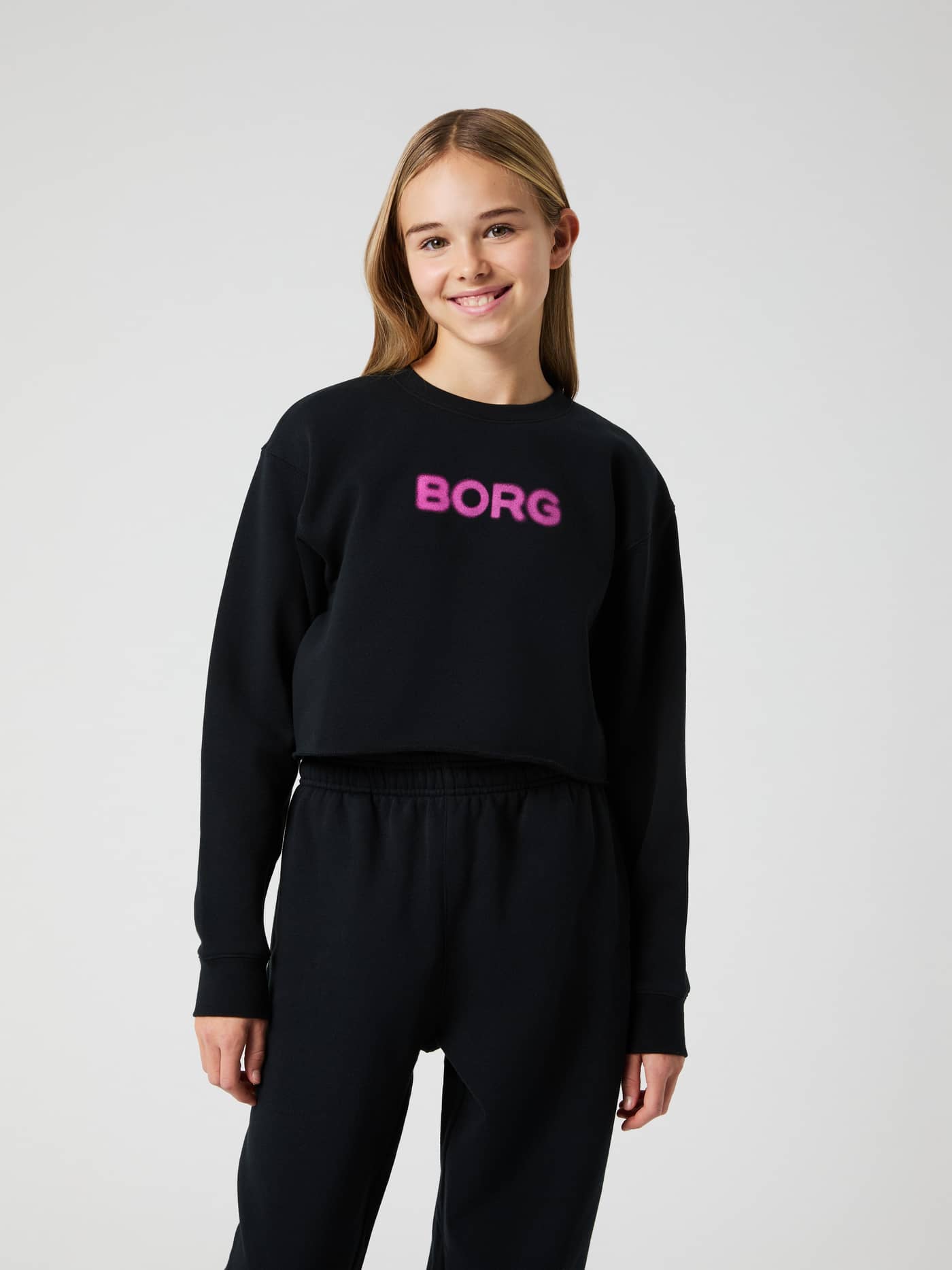 Vista frontal de niña con la Borg Oversized Cropped Sweatshirt en Black Beauty (Negro) y logo rosa para kids. - Image 1