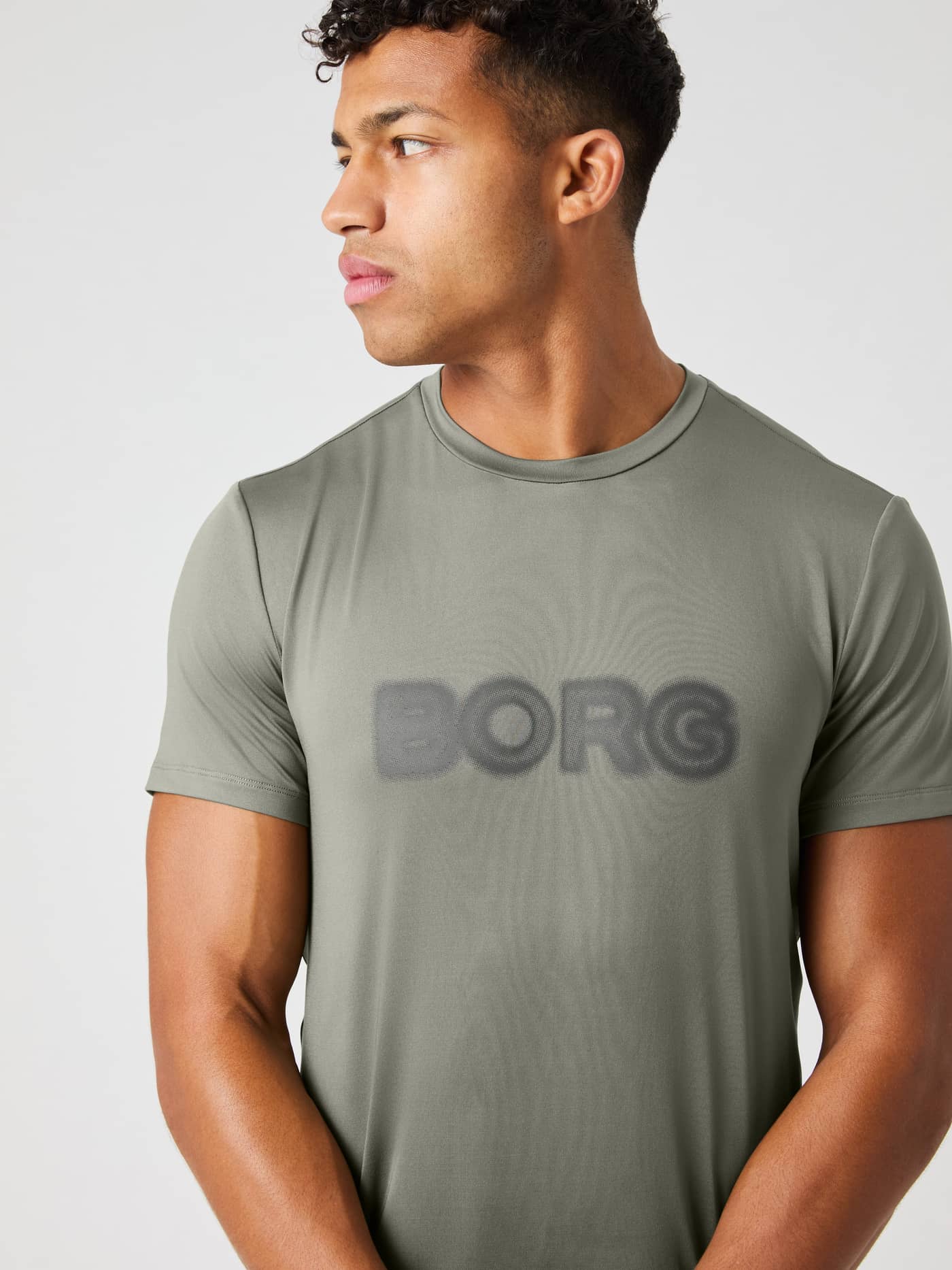 Vorderansicht eines Mannes im Borg Graphic T-Shirt in Dusty Olive (Grün) für das Training mit grauem Grafiklogo. - Image 4