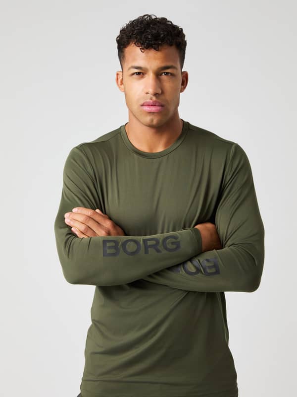 Modell framifrån i Borg Long Sleeve T-Shirt i Forest Night (Grön) med korsade armar som visar logotypen för träning.