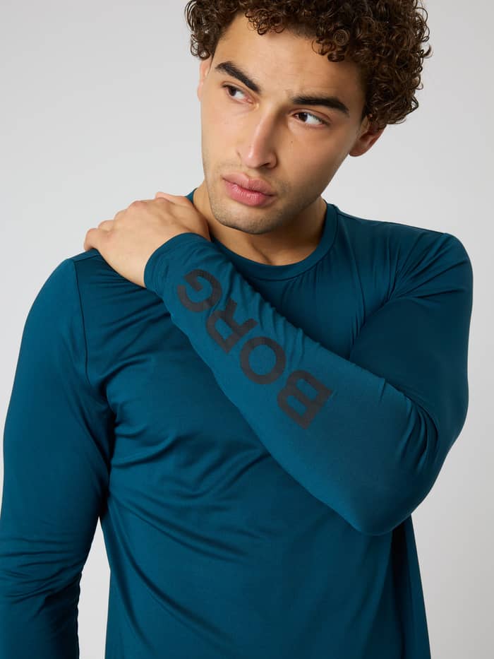 Close-up of the Borg Long Sleeve T-Shirt in Reflecting Pond (Green) with a black logo on the sleeve for men's training.