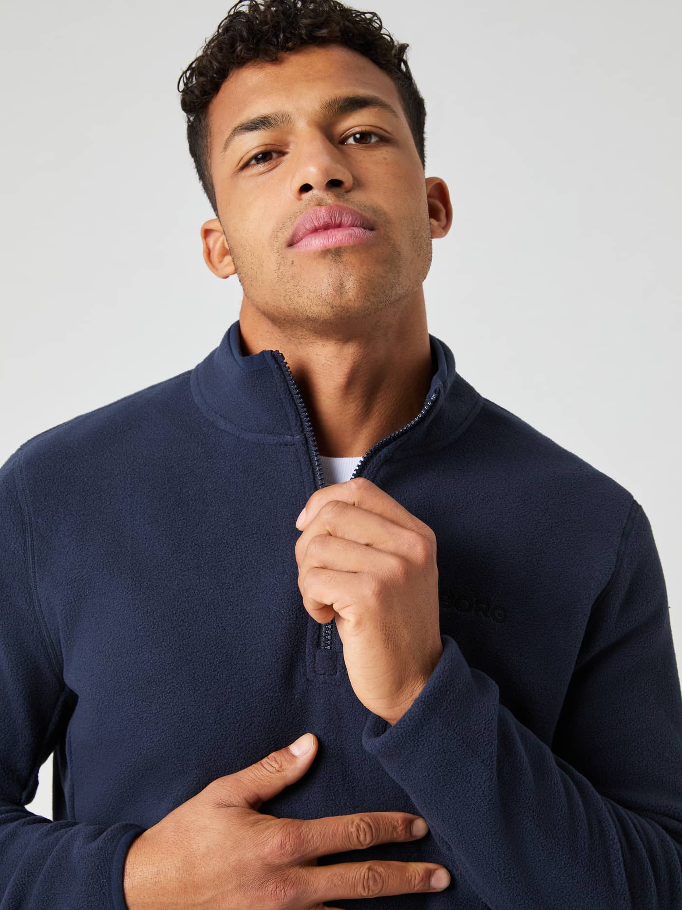 Närbild på modell i Night Sky (Marinblå) Borg Half Zip Fleece som håller i dragkedjan vid kragen för stil och funktion. - Image 1