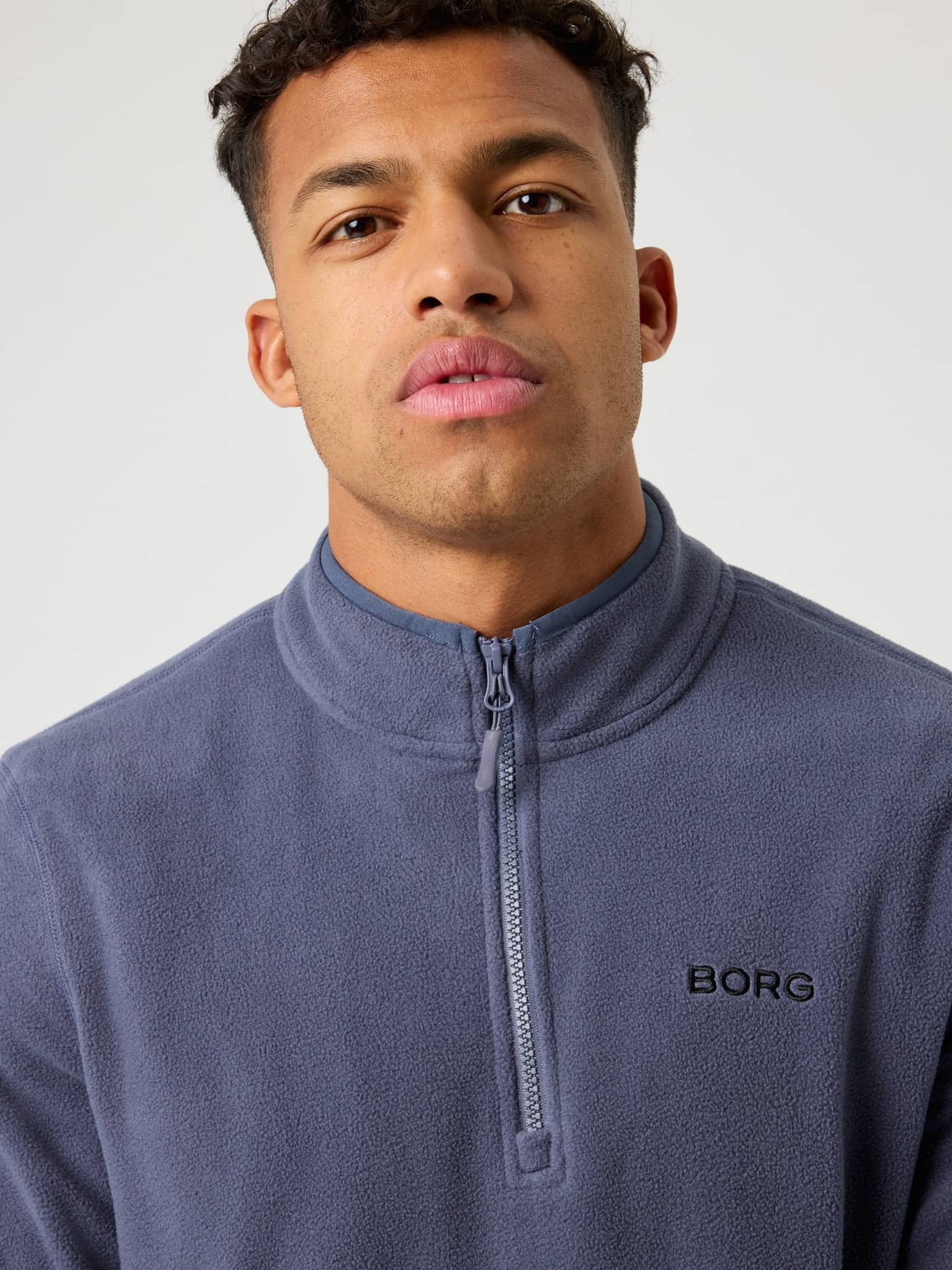 Detailed close-up of the Borg Half Zip Fleece in Odyssey Gray (blue), featuring a functional zip and black chest logo. - Image 5