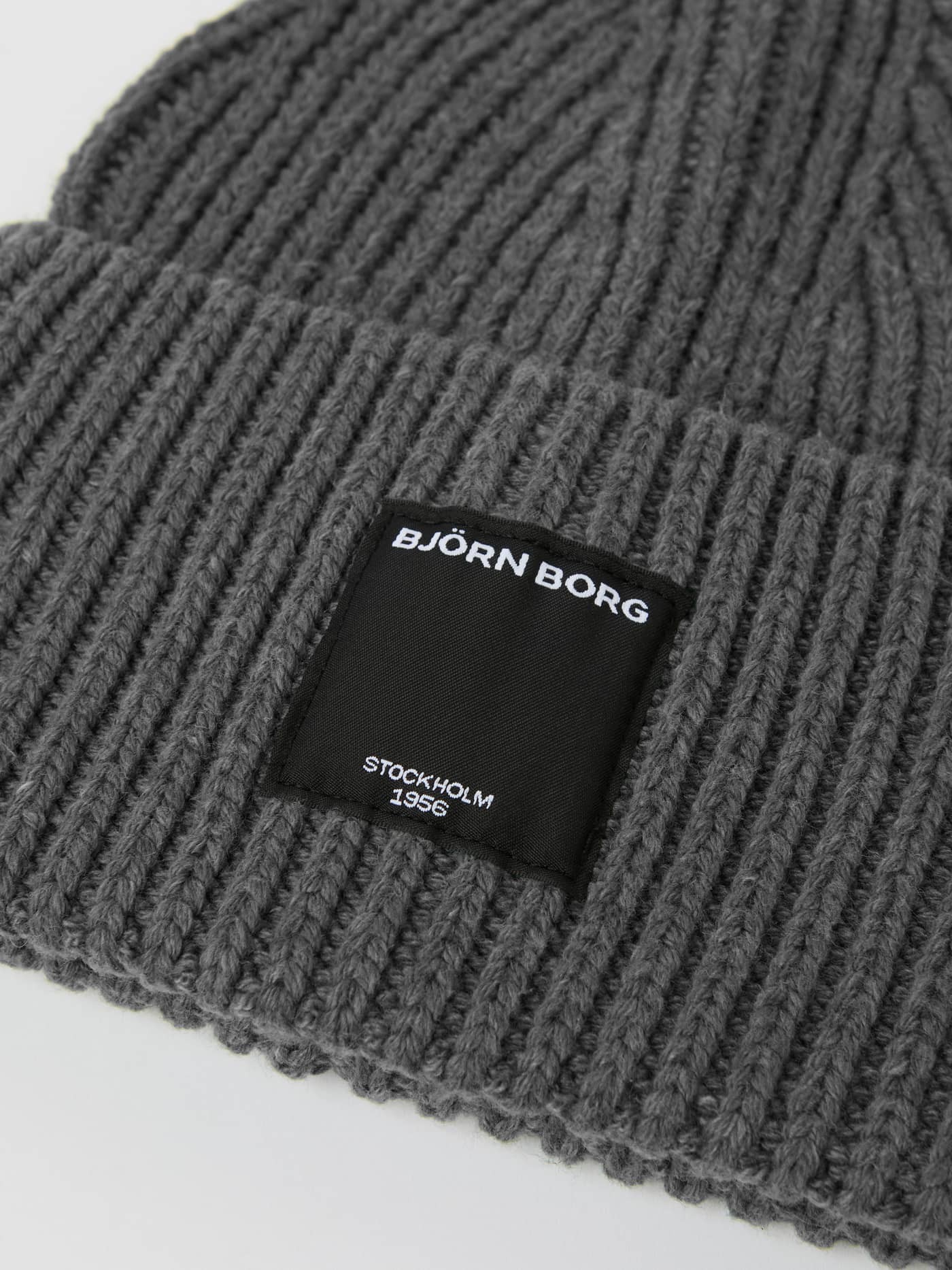 Close-up of the Centre Knit Beanie in Asphalt (Grey) featuring a ribbed texture and black label with a white logo. - Image 2