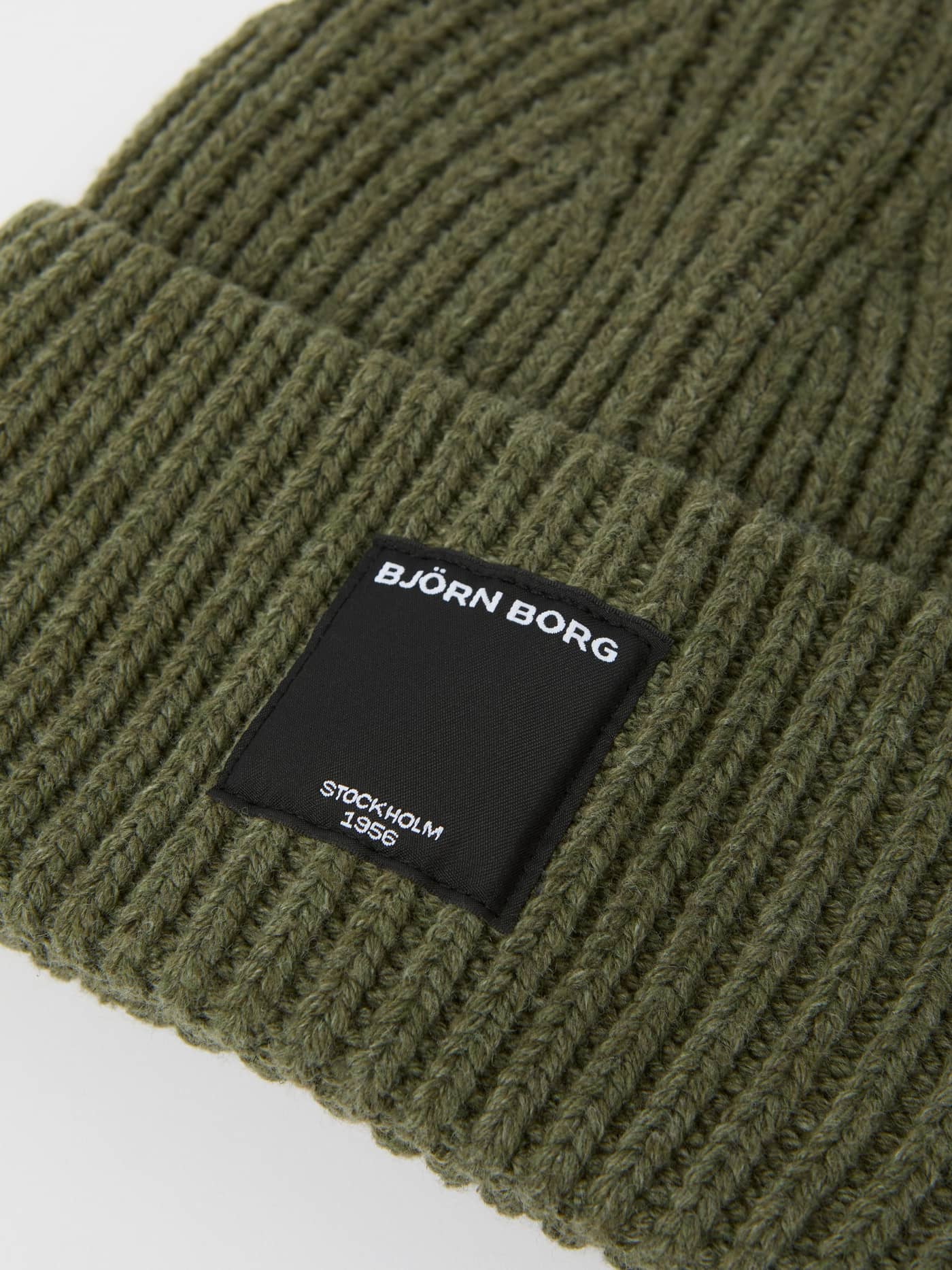 Gros plan du Centre Knit Beanie surdimensionné en Dusty Olive (Vert) avec texture côtelée et étiquette frontale noire. - Image 2