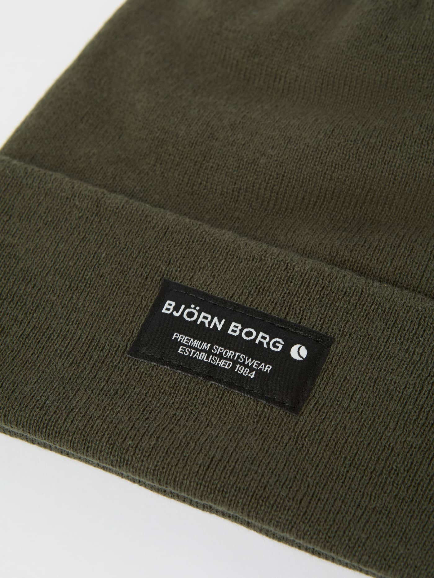 Nærbilde av Forest Night (Grønn) Centre Beanie i økologisk bomull med svart merkelapp og hvit logo på oppbretten. - Image 2