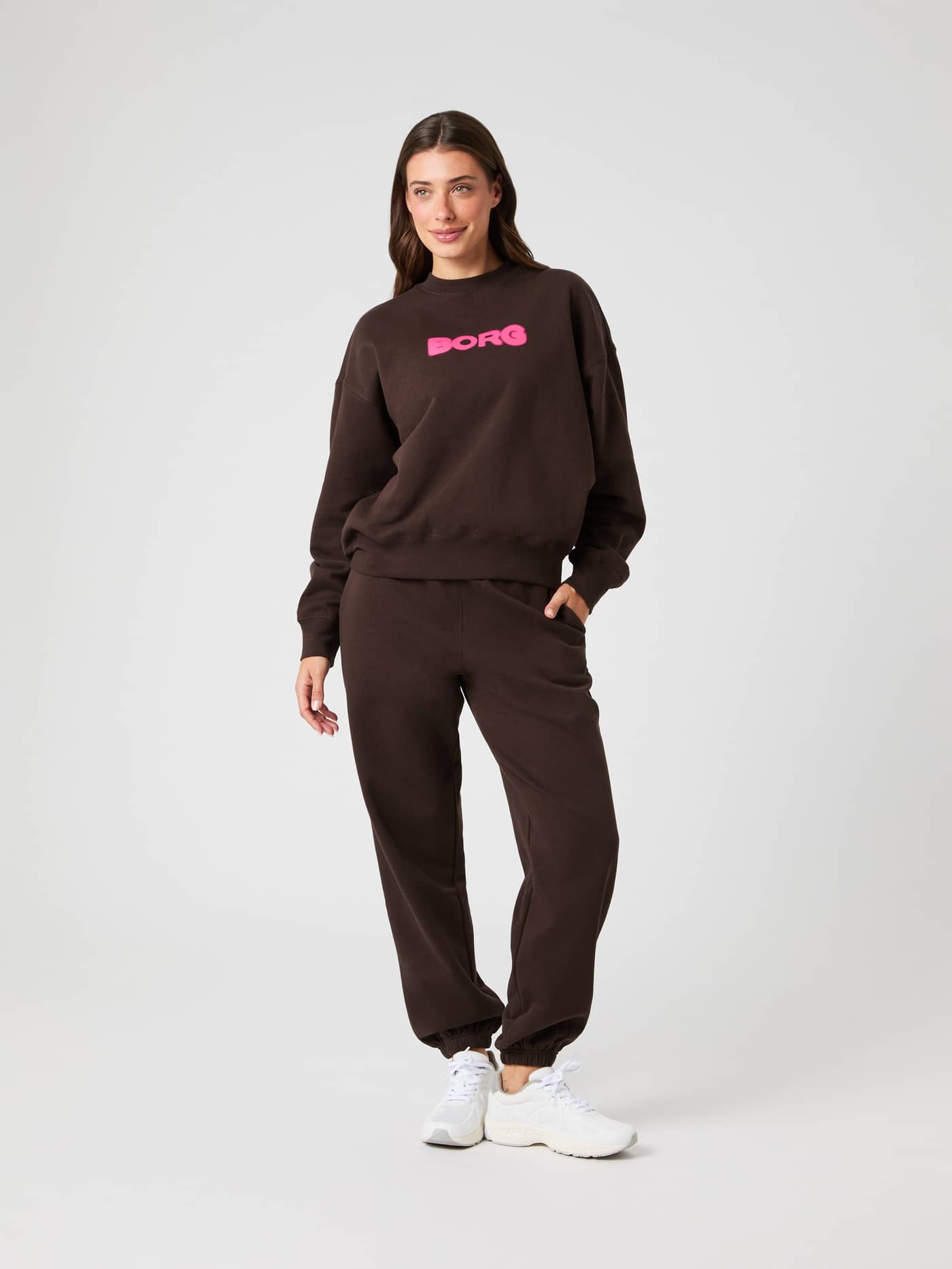 Vue de face du Studio Oversized Sweatpants Molé (Marron) sur un mannequin avec sweat à logo rose et baskets. - Image 3