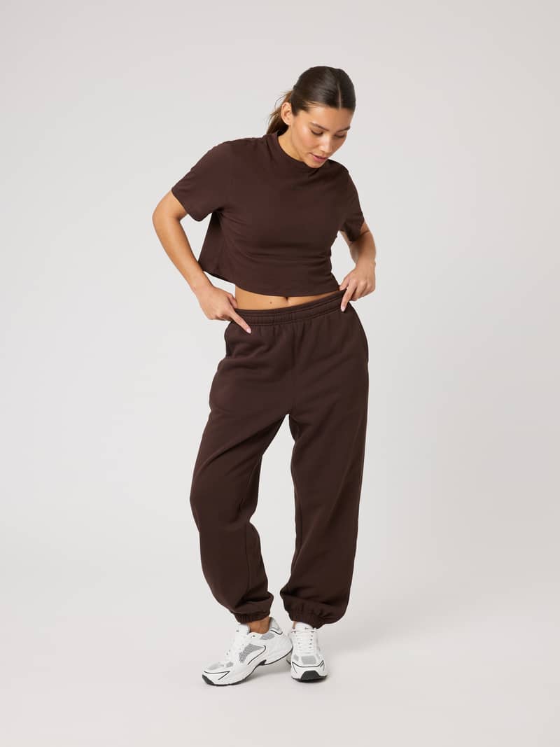 Full-body front view of a model in Studio Oversized Sweatpants in Coffee Bean (Brown) with a relaxed fit and tonal logo.