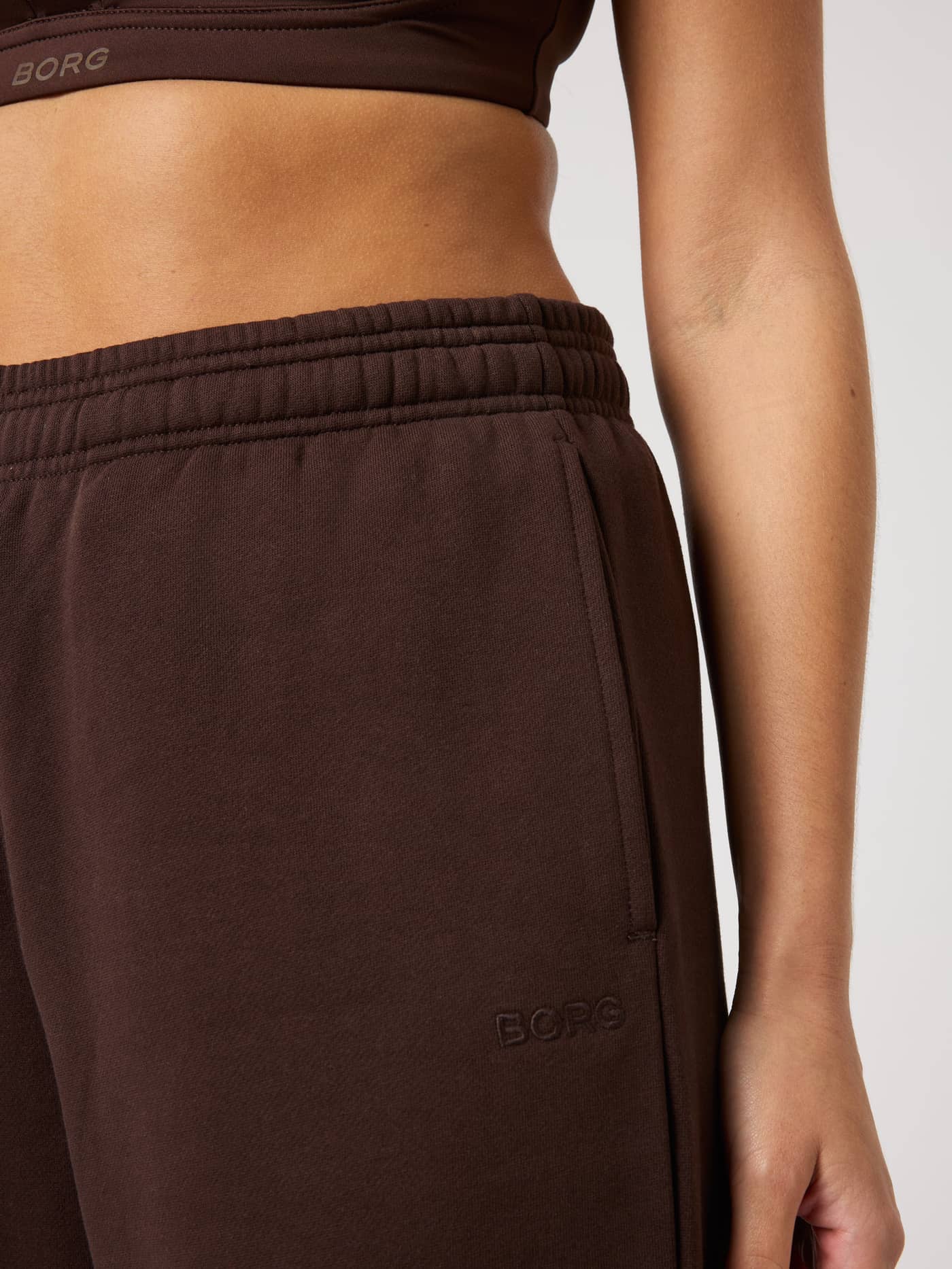 Close-up of Studio Oversized Sweatpants in Coffee Bean (Brown) showing the tonal logo and side pocket detail. - Image 5