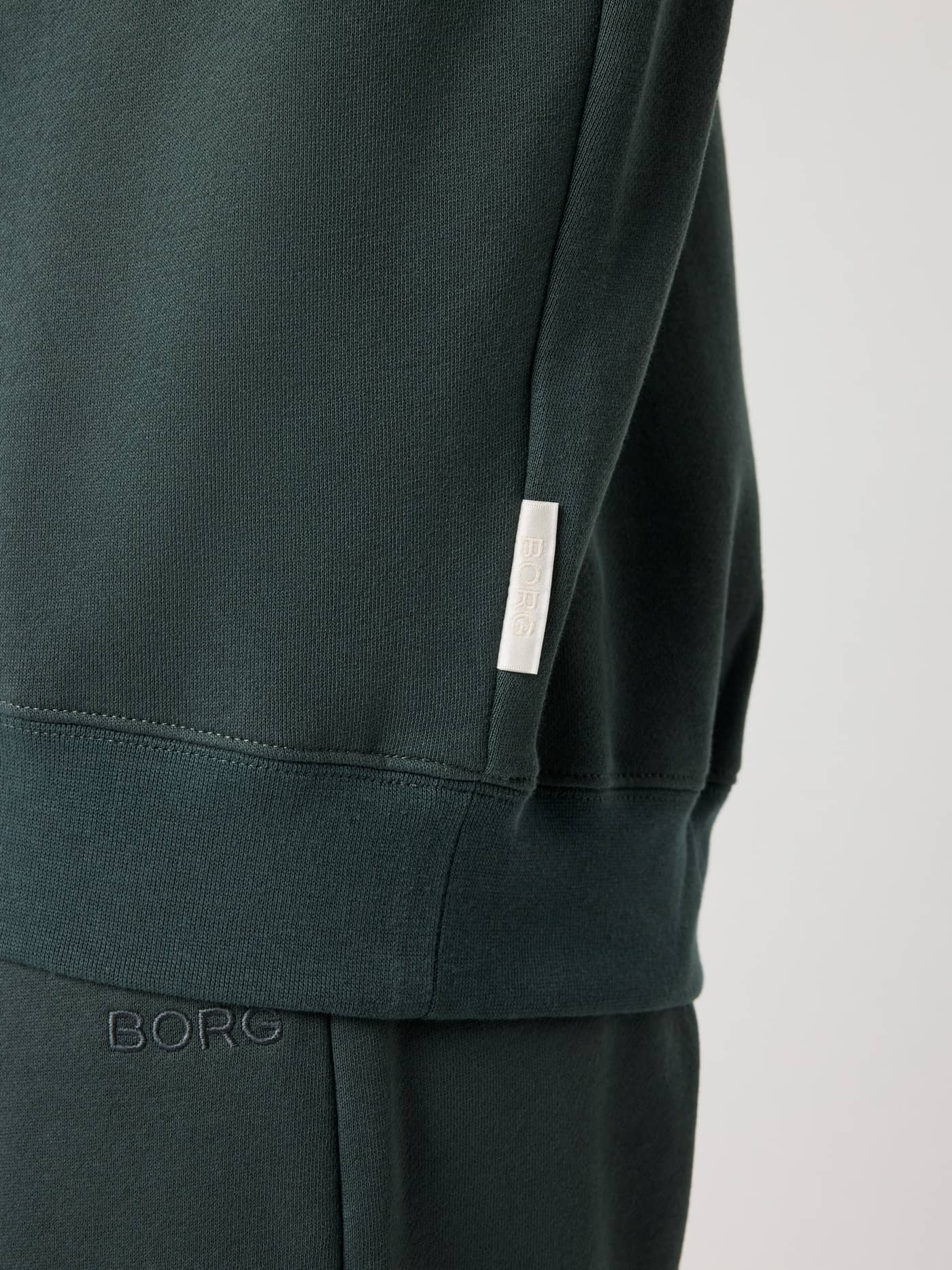 Detailed close-up of the Studio Oversized Hoodie in Urban Chic (Green), showcasing the white BORG logo on the side seam. - Image 5