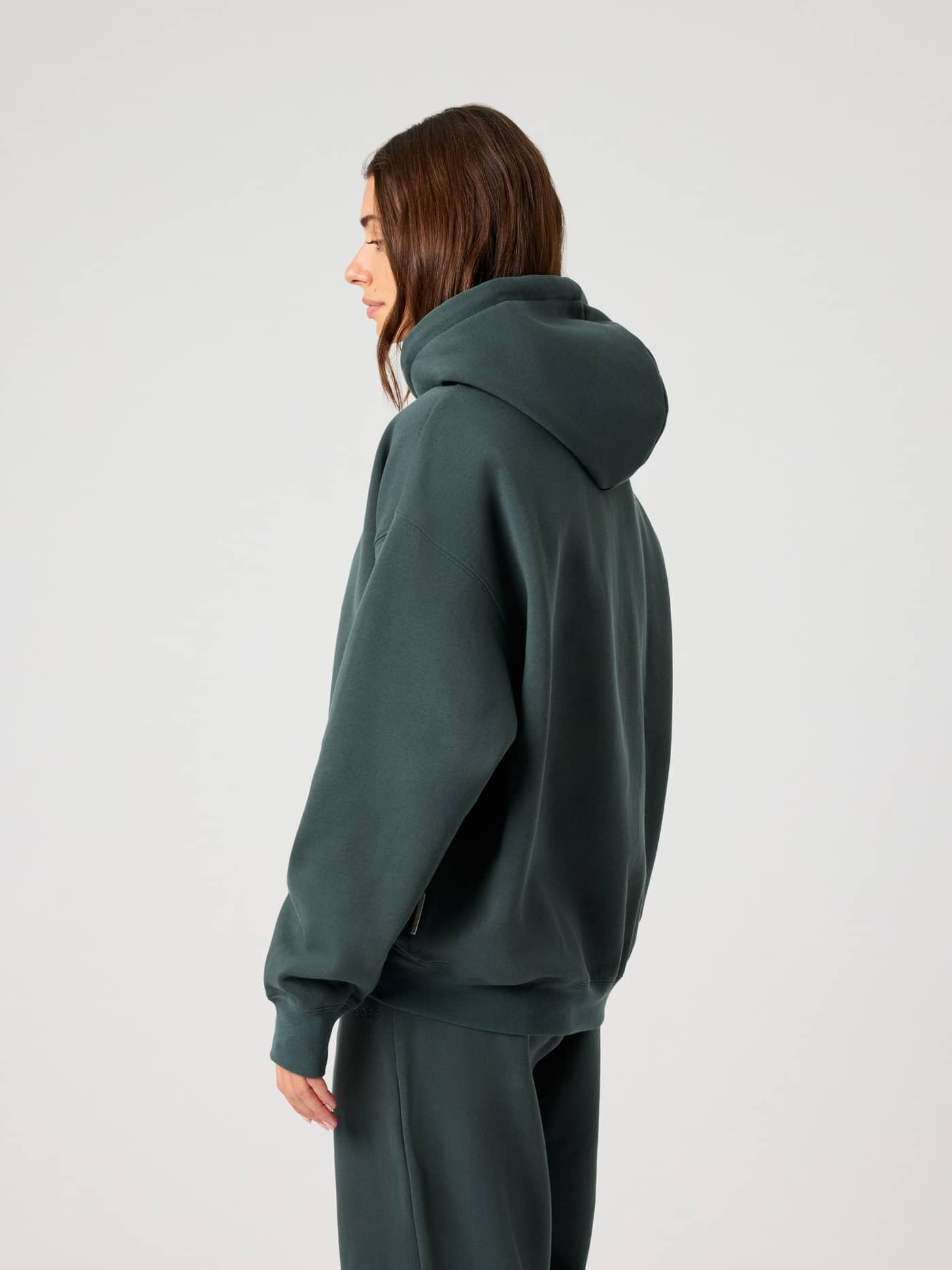 Side view of a woman wearing the Björn Borg Studio Oversized Hoodie in Urban Chic (Green) with a relaxed leisure fit. - Image 2