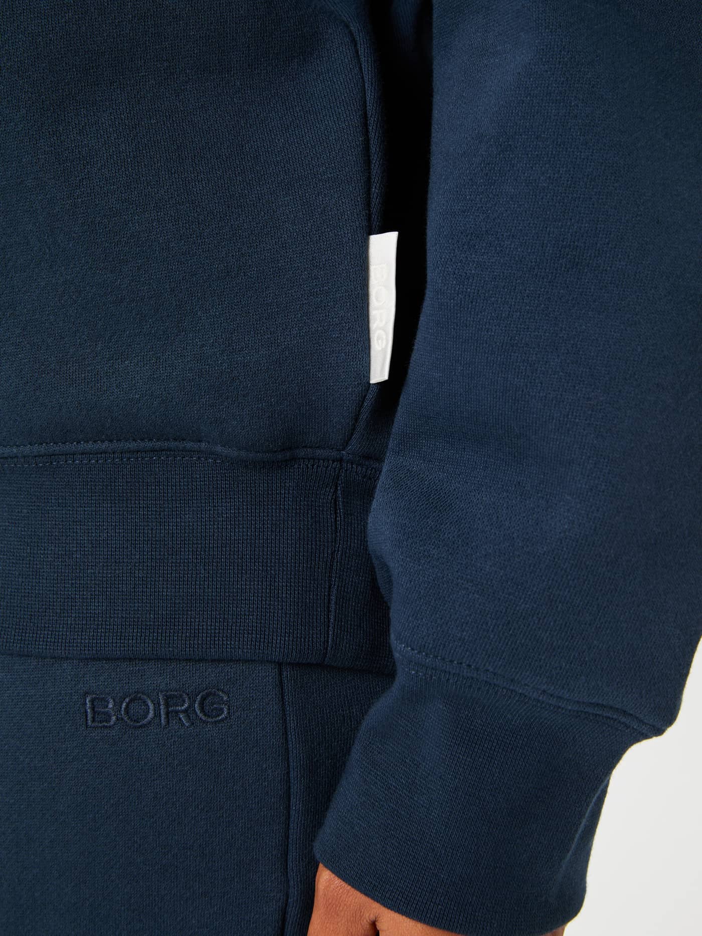 Close-up of the navy blue Studio Oversized Hoodie, highlighting the side seam tag, ribbed hem, and sleeve cuff. - Image 5