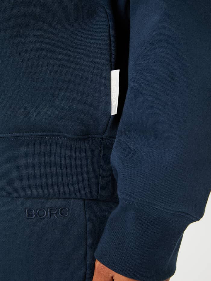 Studio Oversized Hoodie i Outerspace (Marineblå) i nærbillede med hvidt logomærke i siden, ribkant og ærmemanchet. - Image 5