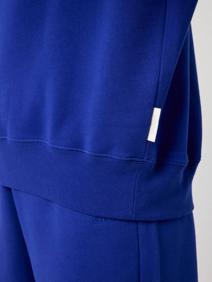 Nahaufnahme des Studio Oversized Sweatshirt in Clematis Blue (Blau) mit kleinem weißem BORG-Label am Saum. - Image 5