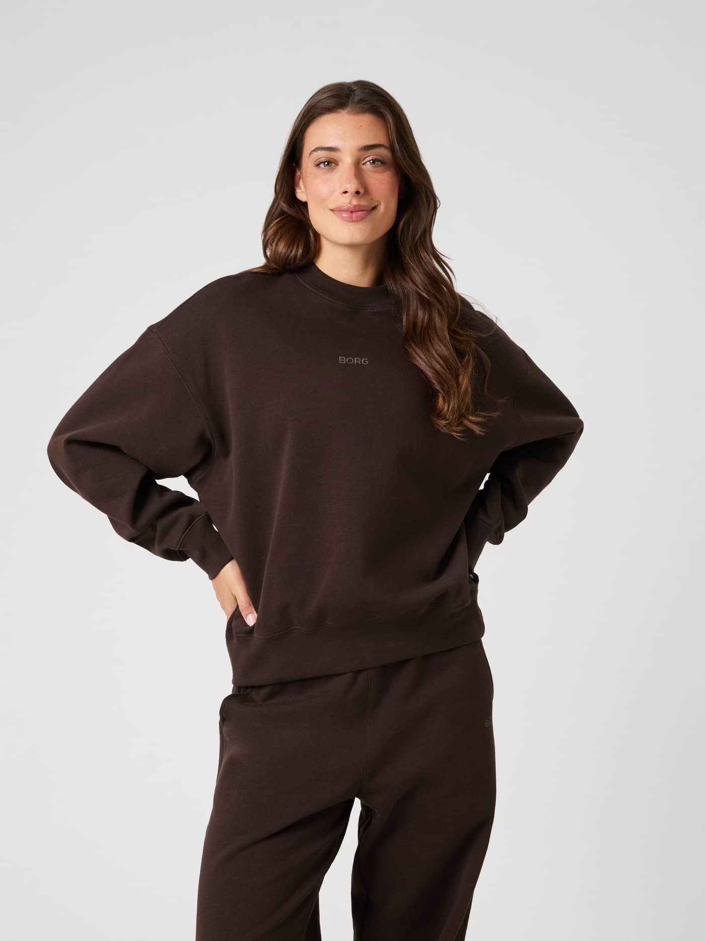 Model seen from the front wearing the brown Studio Oversized Sweatshirt and matching trousers. - Image 1