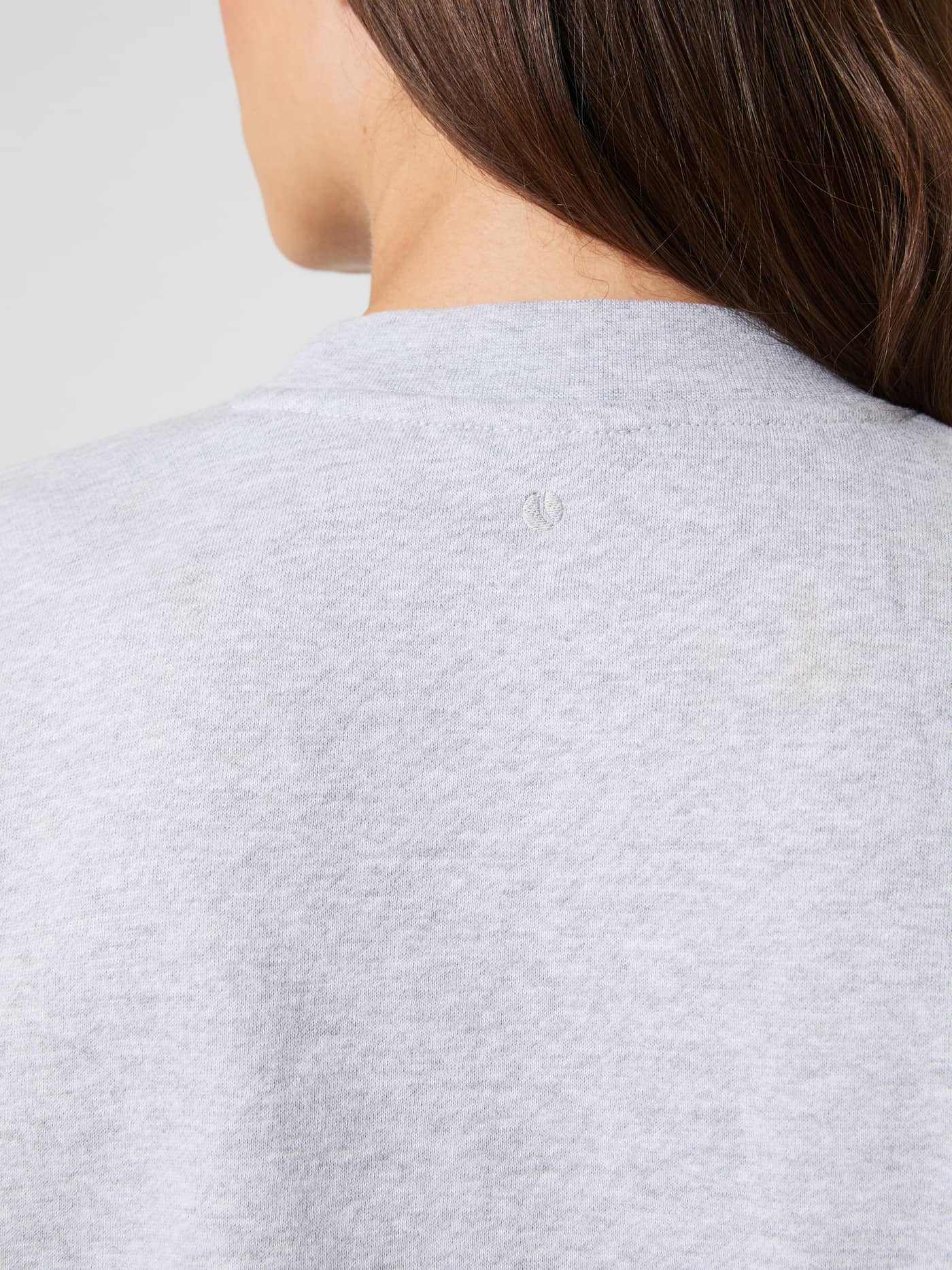 Back detail shot of the women's Studio Oversized Sweatshirt in light grey melange, showing the subtle logo at the neck. - Image 7