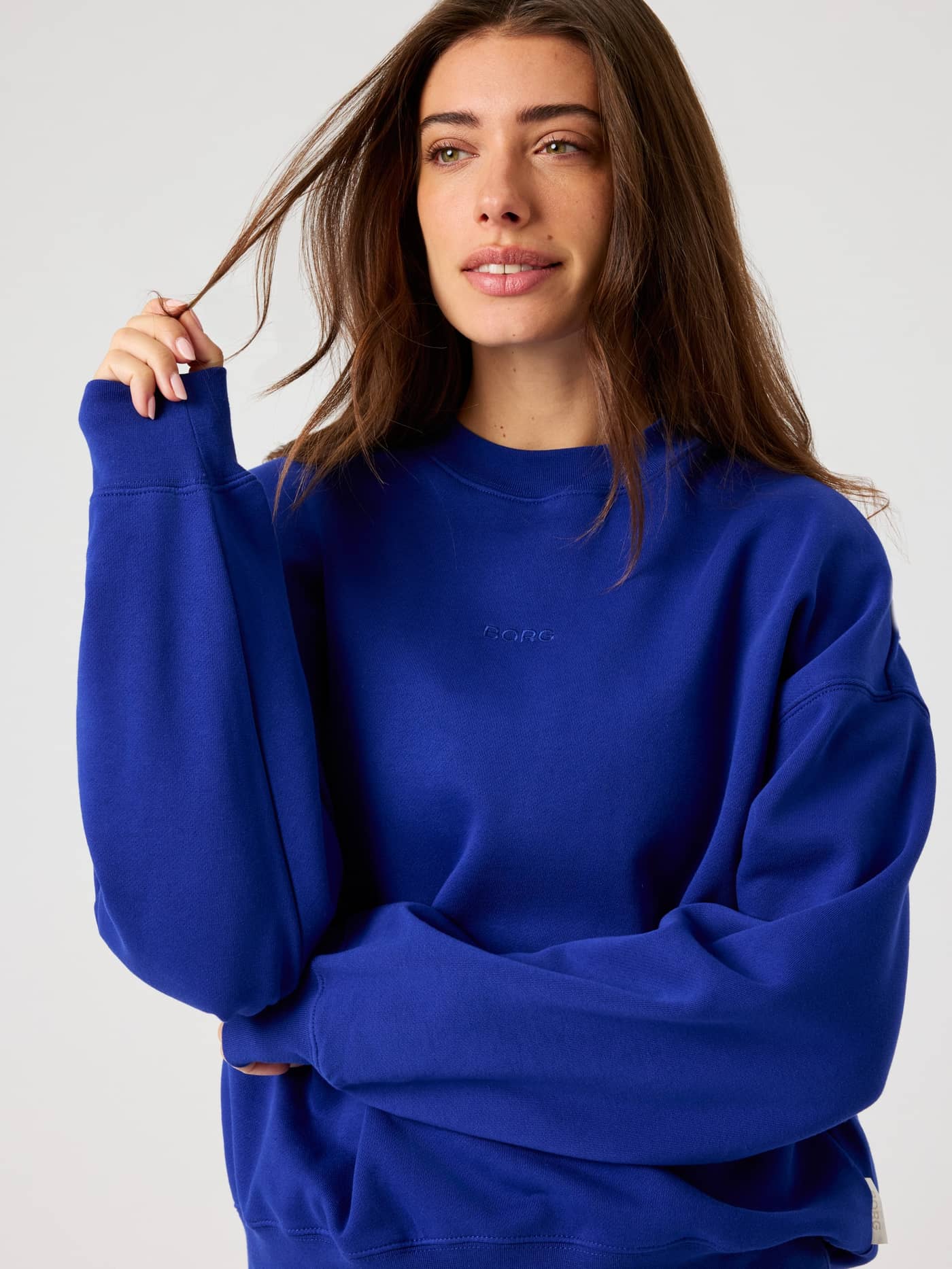 Front view of a woman wearing the Clematis Blue (Blue) Studio Oversized Sweatshirt with a relaxed fit and tonal logo. - Image 4