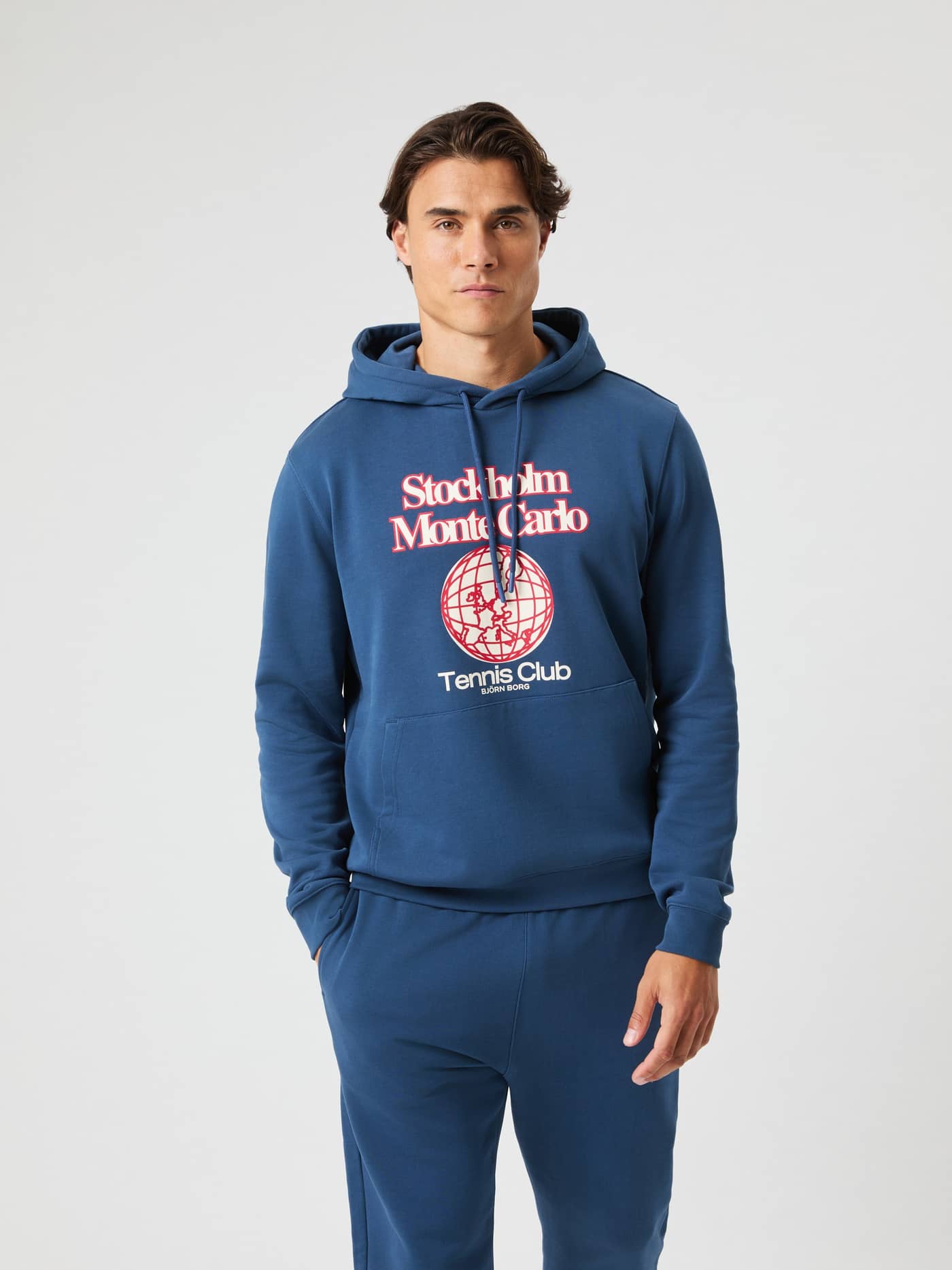 Front view of a man wearing the cotton Borg Classic Print Hoodie in Sargasso Sea (Blue) with a tennis-inspired graphic. - Image 2