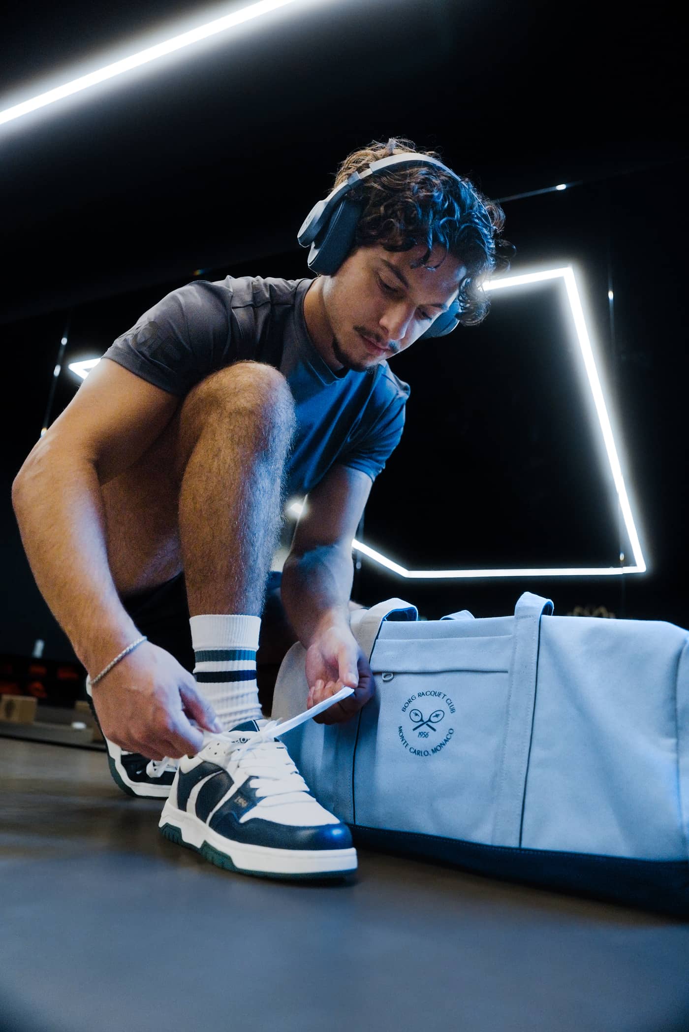 Man tying his off white, navy, and green Björn Borg Men's Ollie Leather Sneakers in a tennis leisure setting. - Image 5