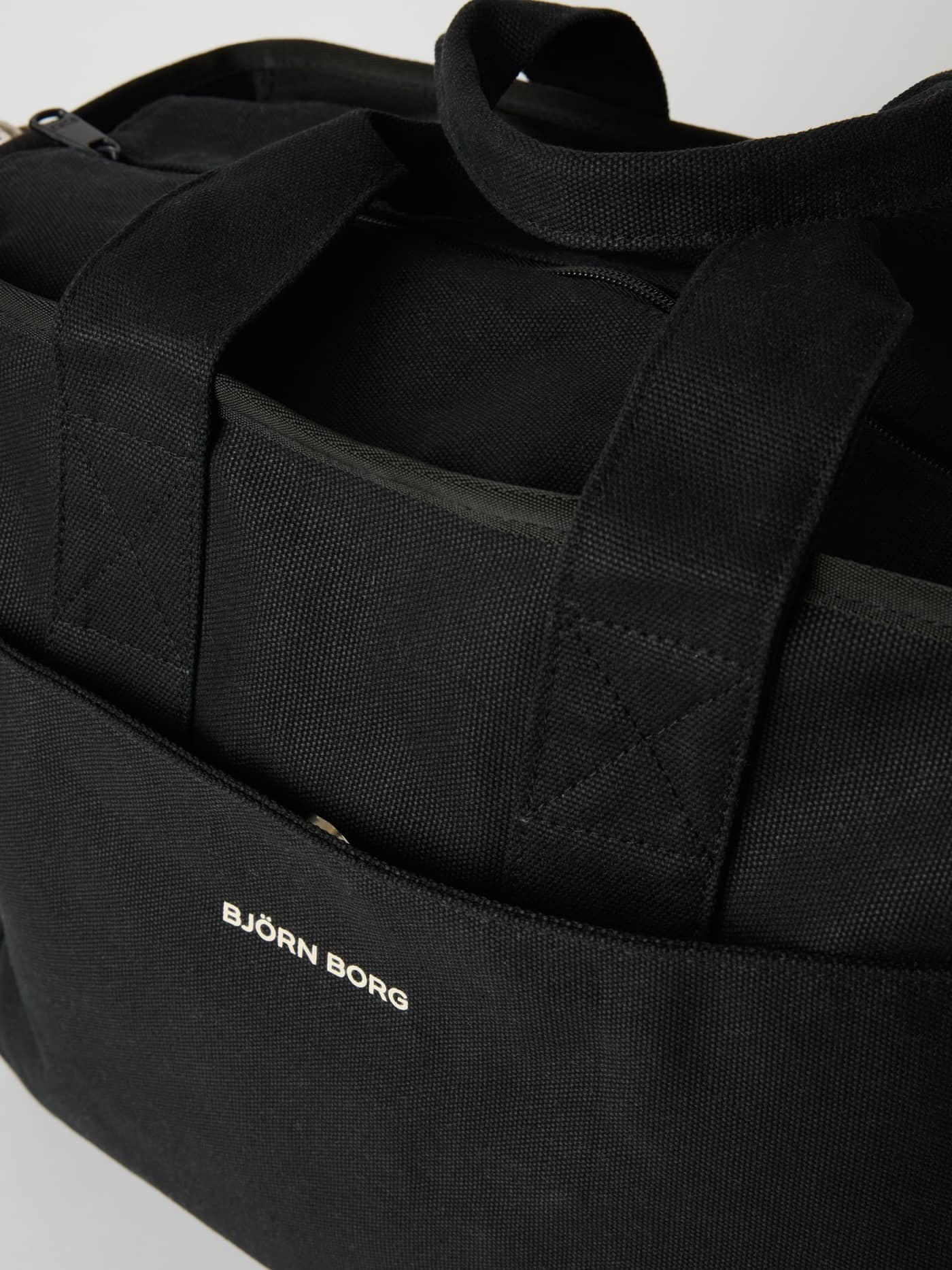 Gedetailleerde close-up van de katoenen Studio Canvas Tote 34L in Black Beauty (Zwart) met een wit logo. - Image 3