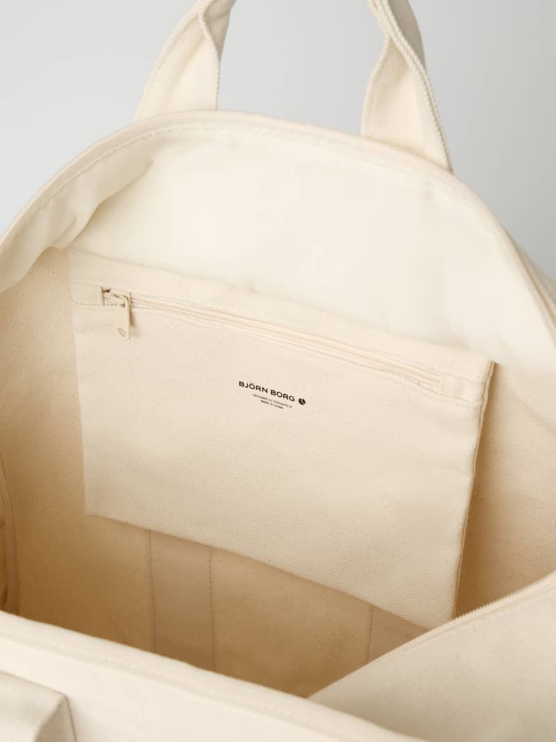 Vue intérieure du Studio Canvas Tote 34L en Egret (Blanc) montrant la matière en coton et la poche zippée. - Image 5