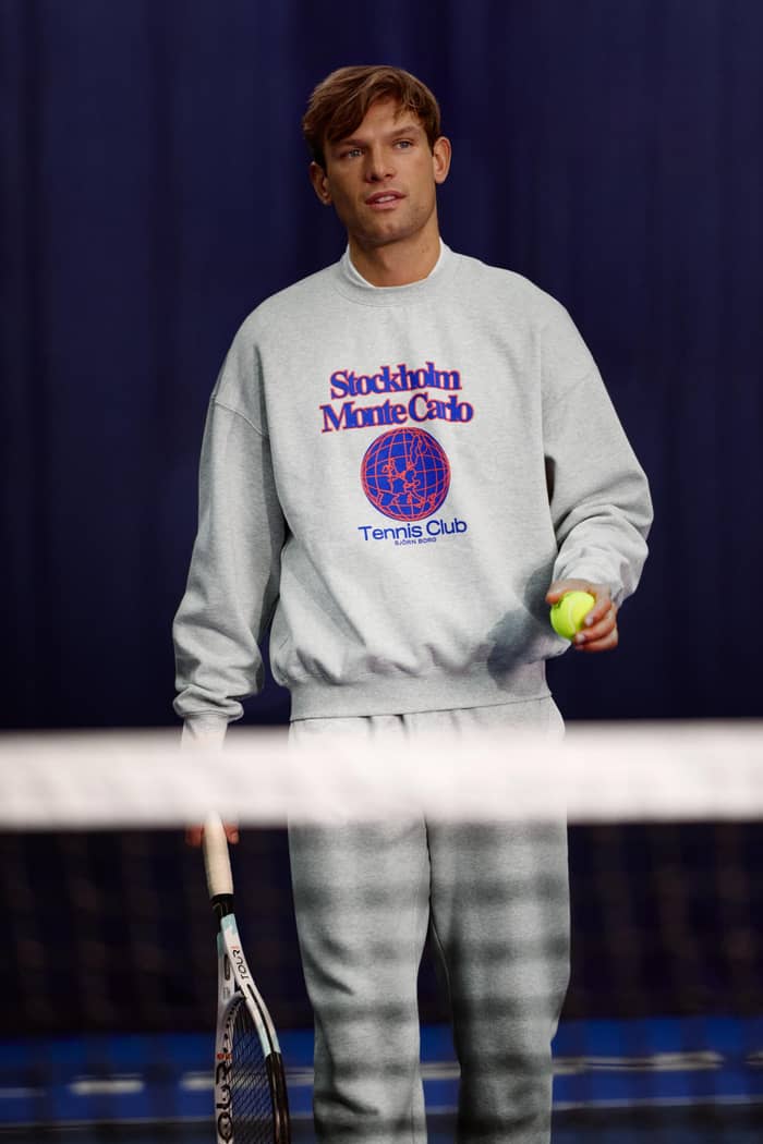 Vooraanzicht van een man op een tennisbaan in het grijze Borg Oversized Sweatshirt met rood-blauw tennislogo. - Image 2