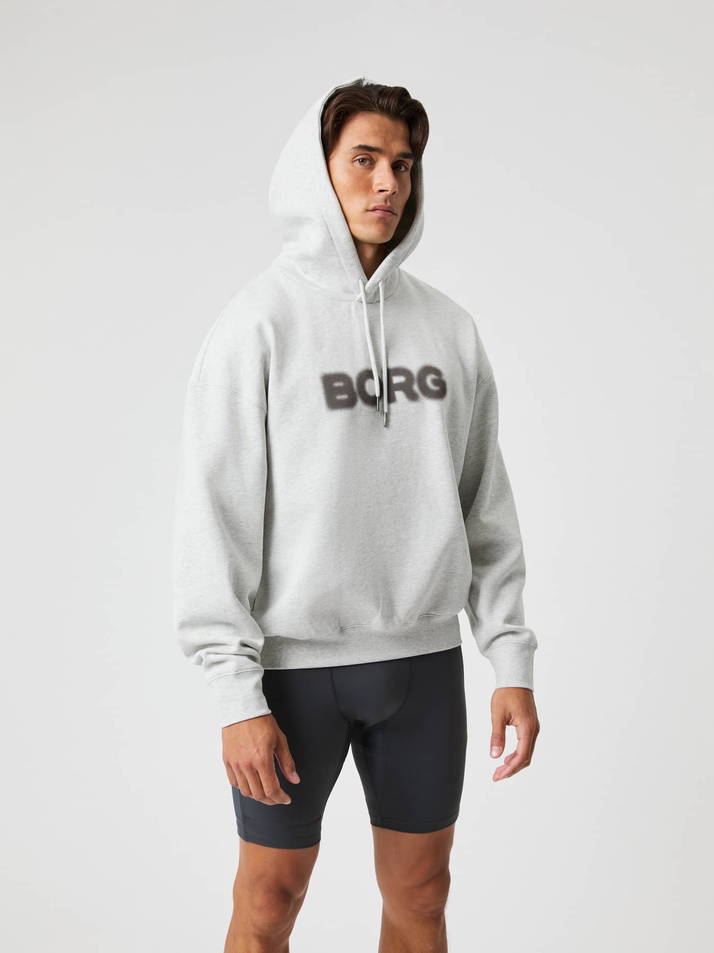 Vista frontal de un hombre con la Borg Oversized Hoodie en Ultra Light Grey Melange (Gris), logo negro y ajuste relajado. - Image 8