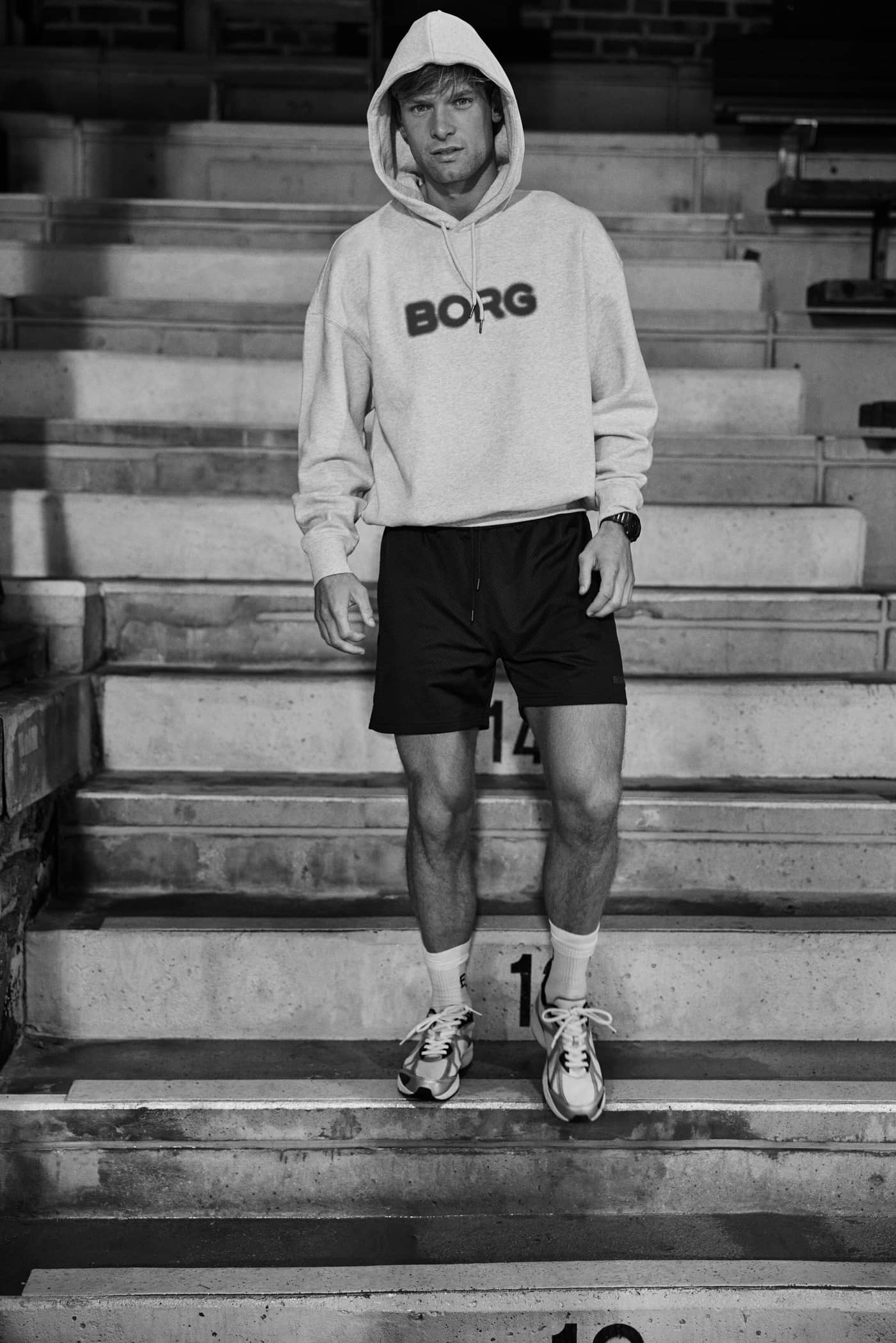 Vista frontal de un hombre en escaleras con la Borg Oversized Hoodie en Ultra Light Grey Melange (Gris) y logo negro. - Image 4