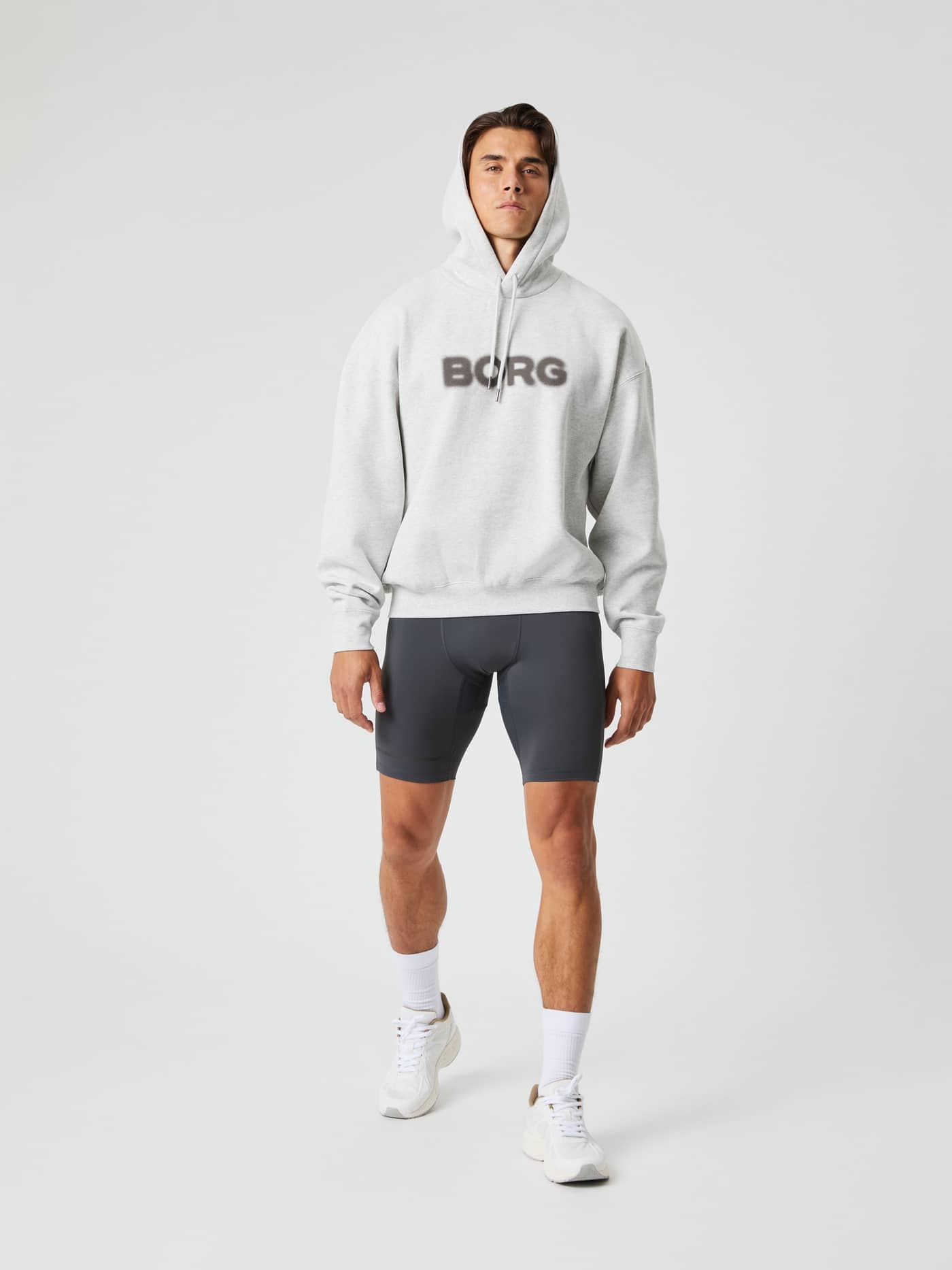 Vista frontal de cuerpo completo de un hombre con la Borg Oversized Hoodie en Ultra Light Grey Melange (Gris) y logo oscuro. - Image 7