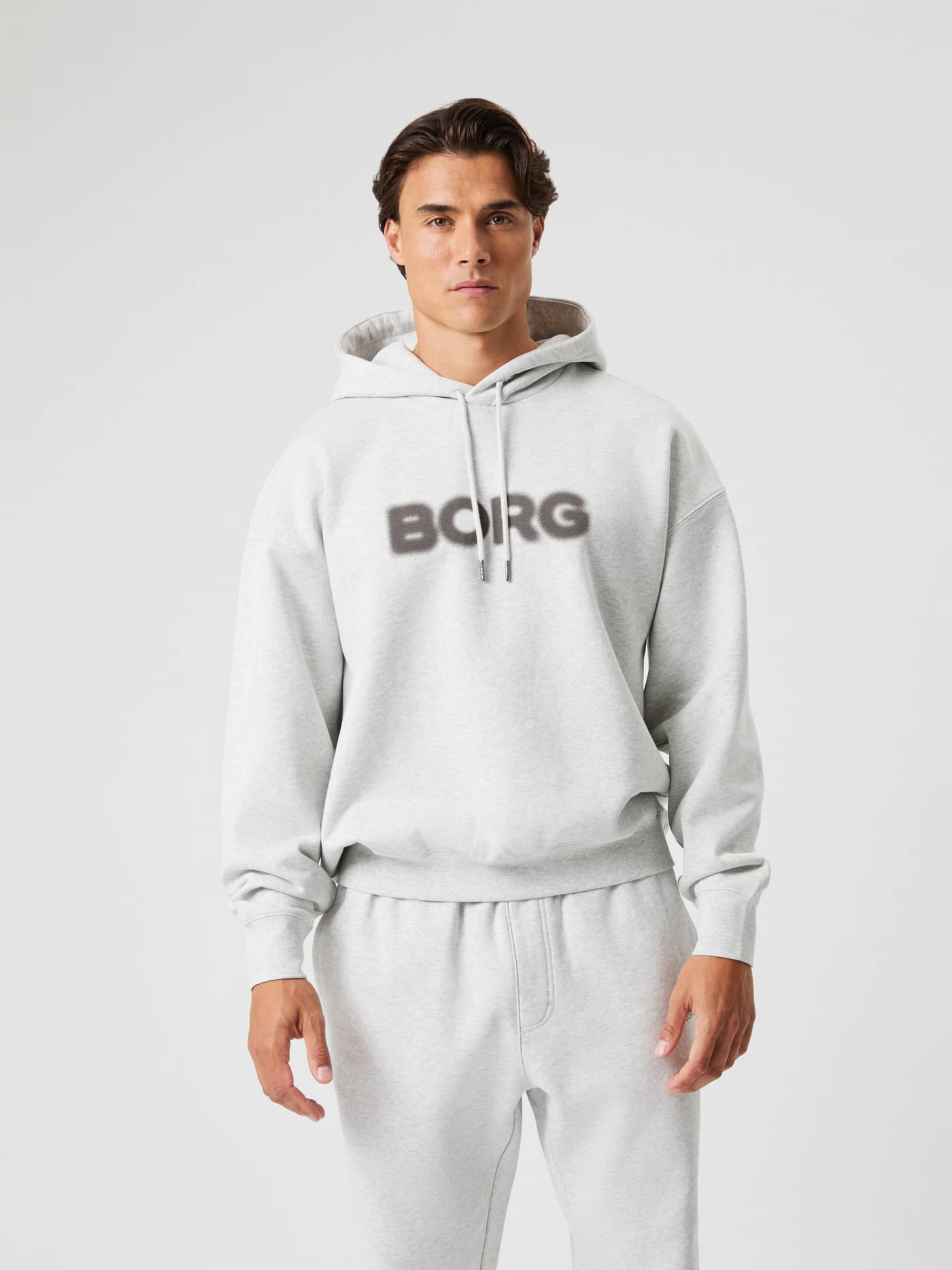 Vista frontal de un hombre con la Borg Oversized Hoodie en Ultra Light Grey Melange (Gris) con logo efecto spray oscuro. - Image 3