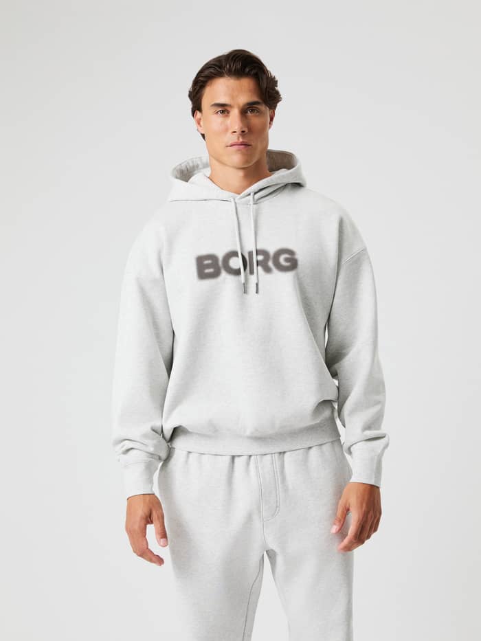 Front view of a man wearing the Borg Oversized Hoodie in Ultra Light Grey Melange (Grey) with a dark spray effect logo.