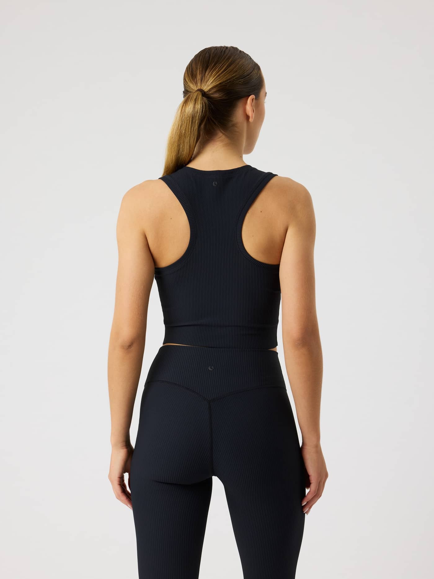 Rückansicht eines Models im Studio Ribbed Cropped Tank Top in Black Beauty (Schwarz) für das Training. - Image 5