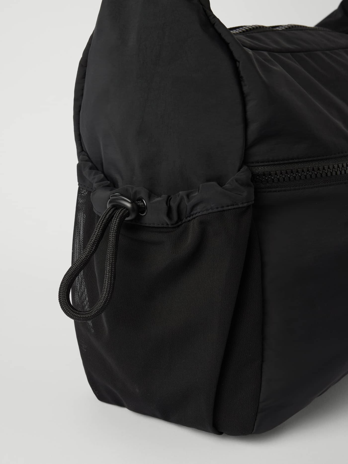 Detaljerad sidovy av Studio Shoulder Bag 18L i Black Beauty (Svart) med en nätficka med dragsko för träning. - Image 3
