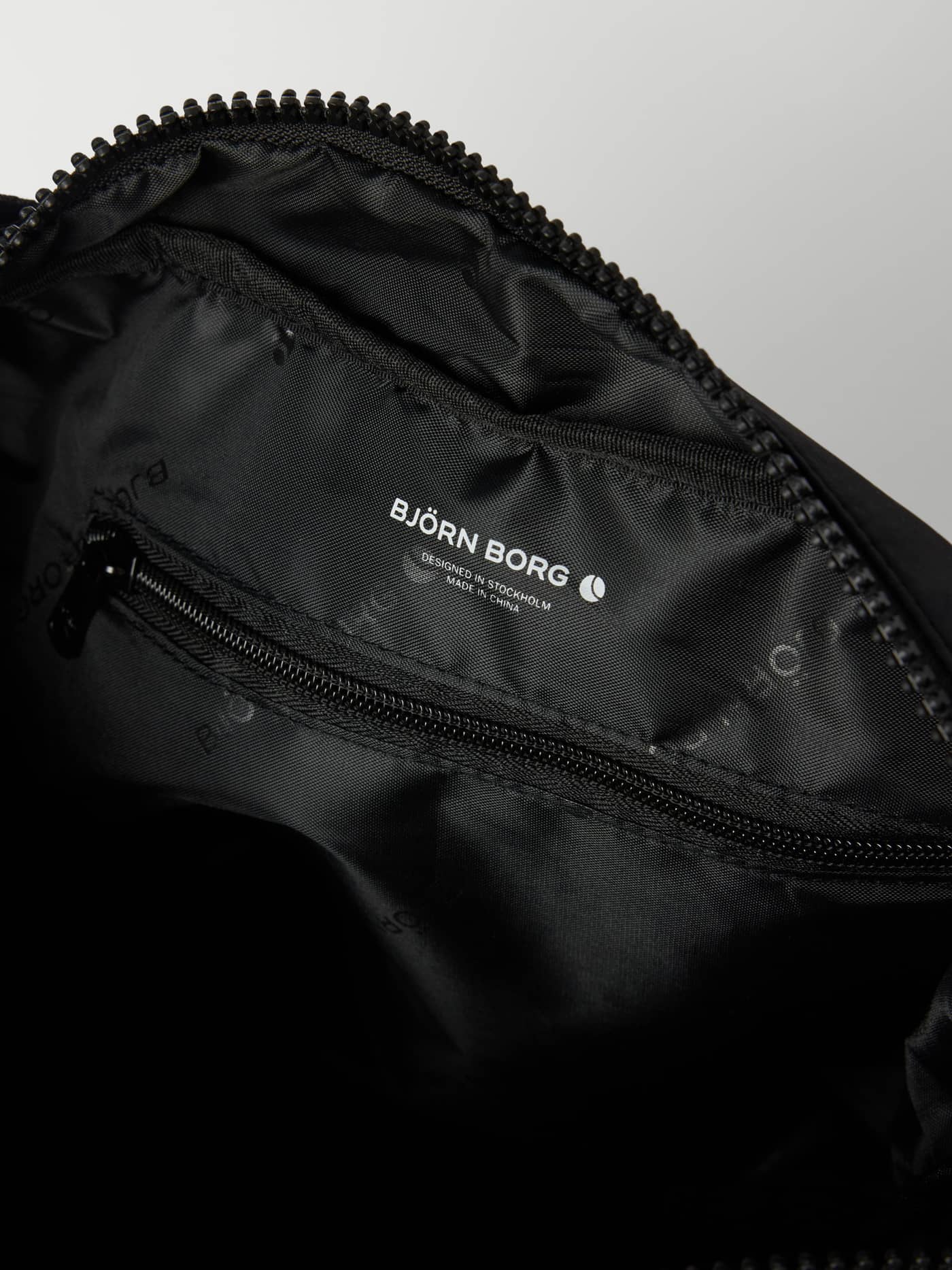 Insidan av Studio Shoulder Bag 18L i Black Beauty (Svart) med vit logotyp och innerficka med dragkedja för träning. - Image 4