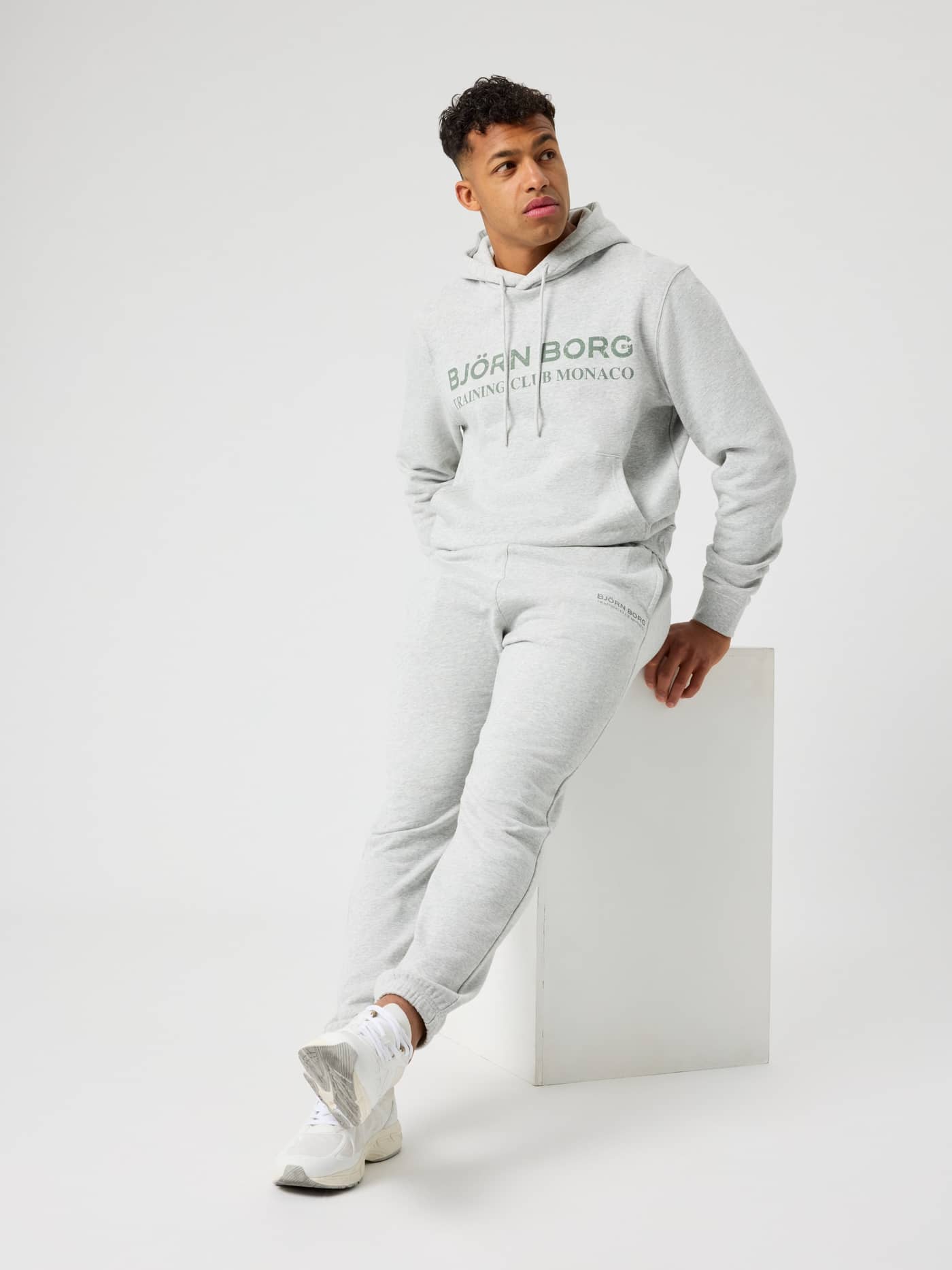 Sittande man i Borg Classic Print Hoodie i Ultra Light Grey Melange (Grå) med ett träningsklubbstryck för tennis. - Image 5