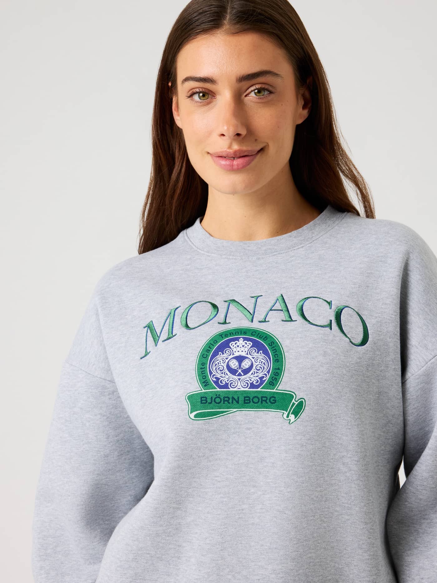 Front close-up of a woman wearing the Björn Borg Boyfriend Sweatshirt in Light Grey Melange (Grey) with a green tennis logo. - Image 5